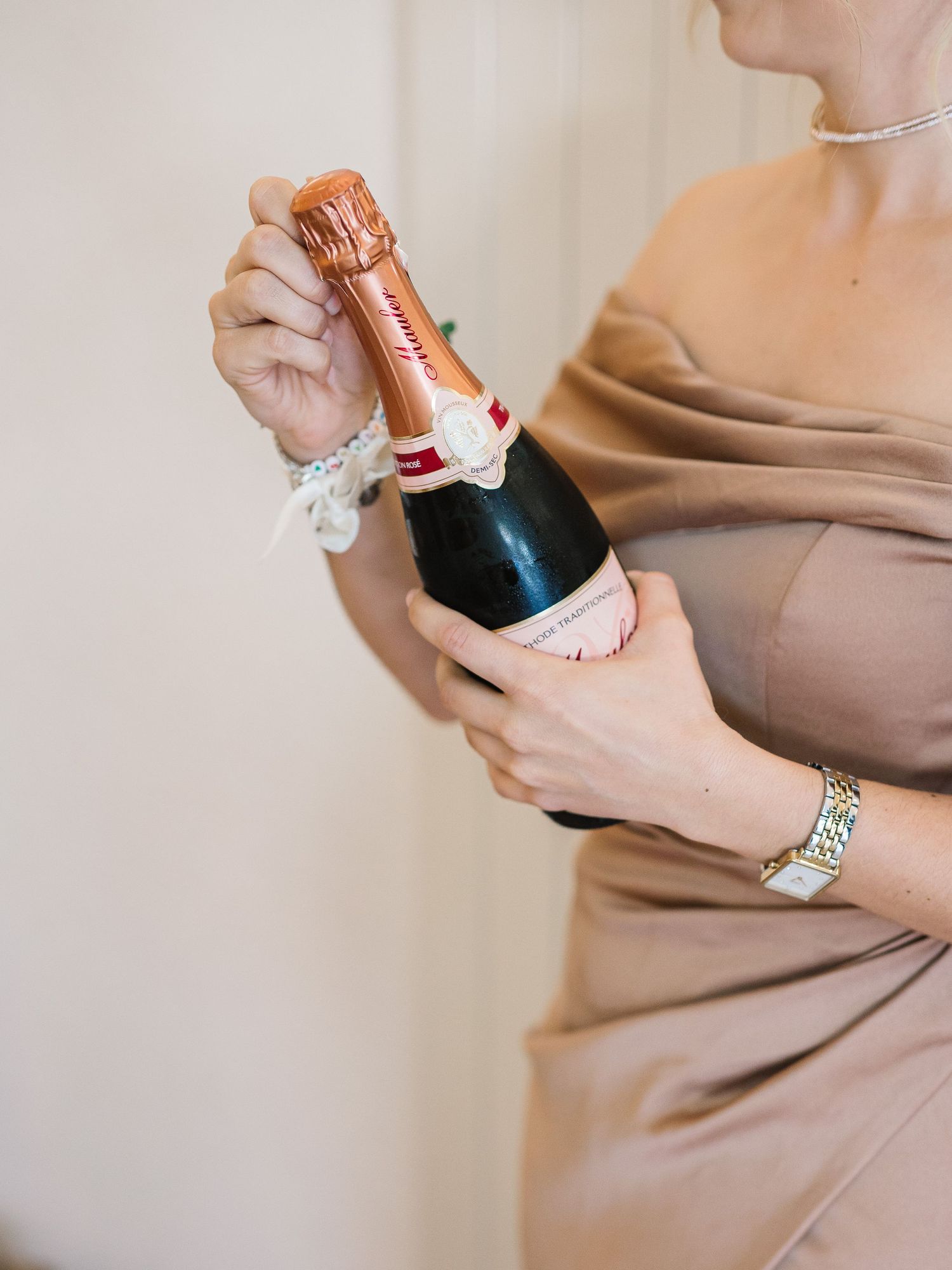 Hands hold champagne bottles during wedding preparations in neutral tones.