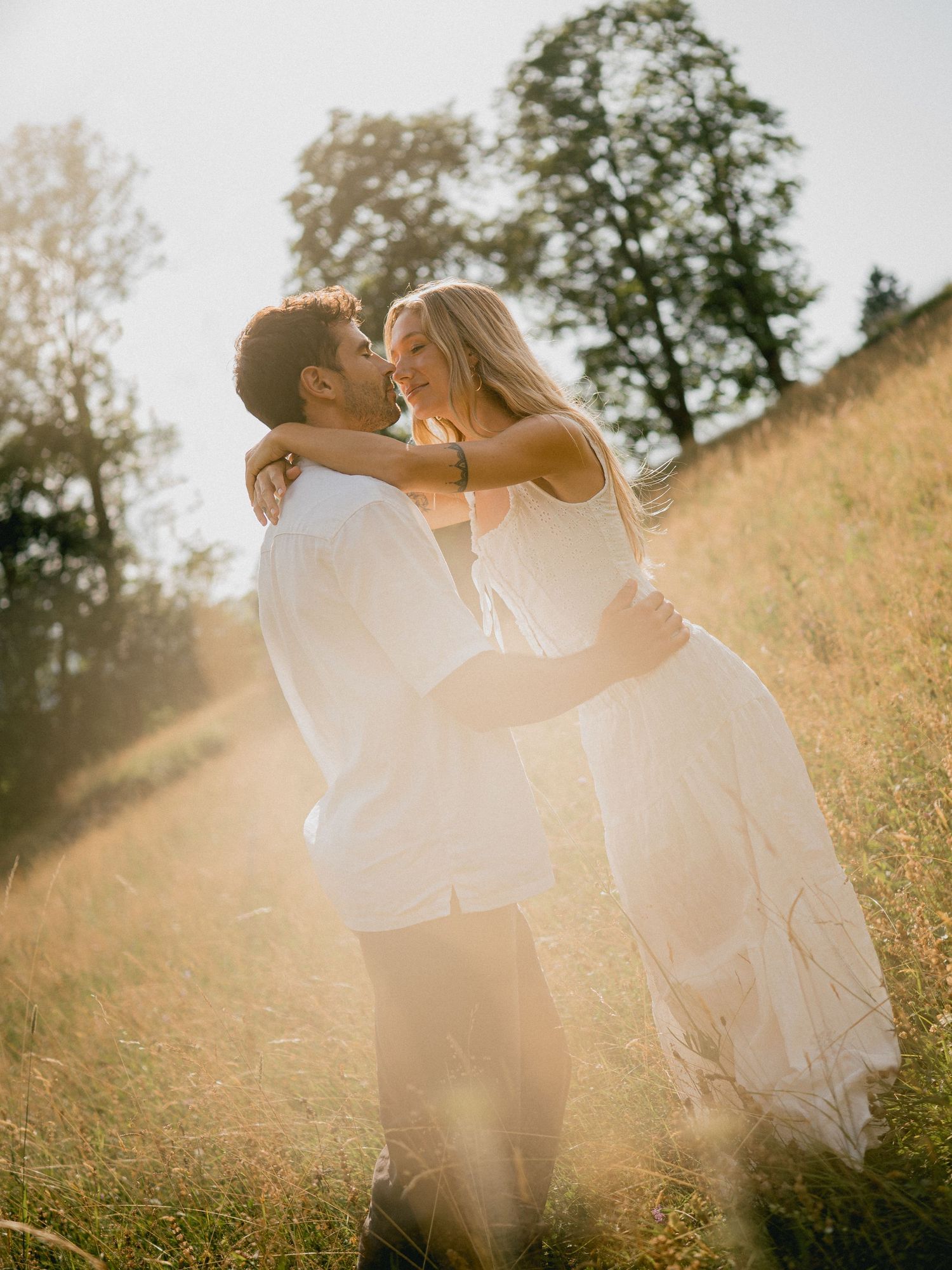 Romantic couple in white clothing embracing in a sunlit meadow.