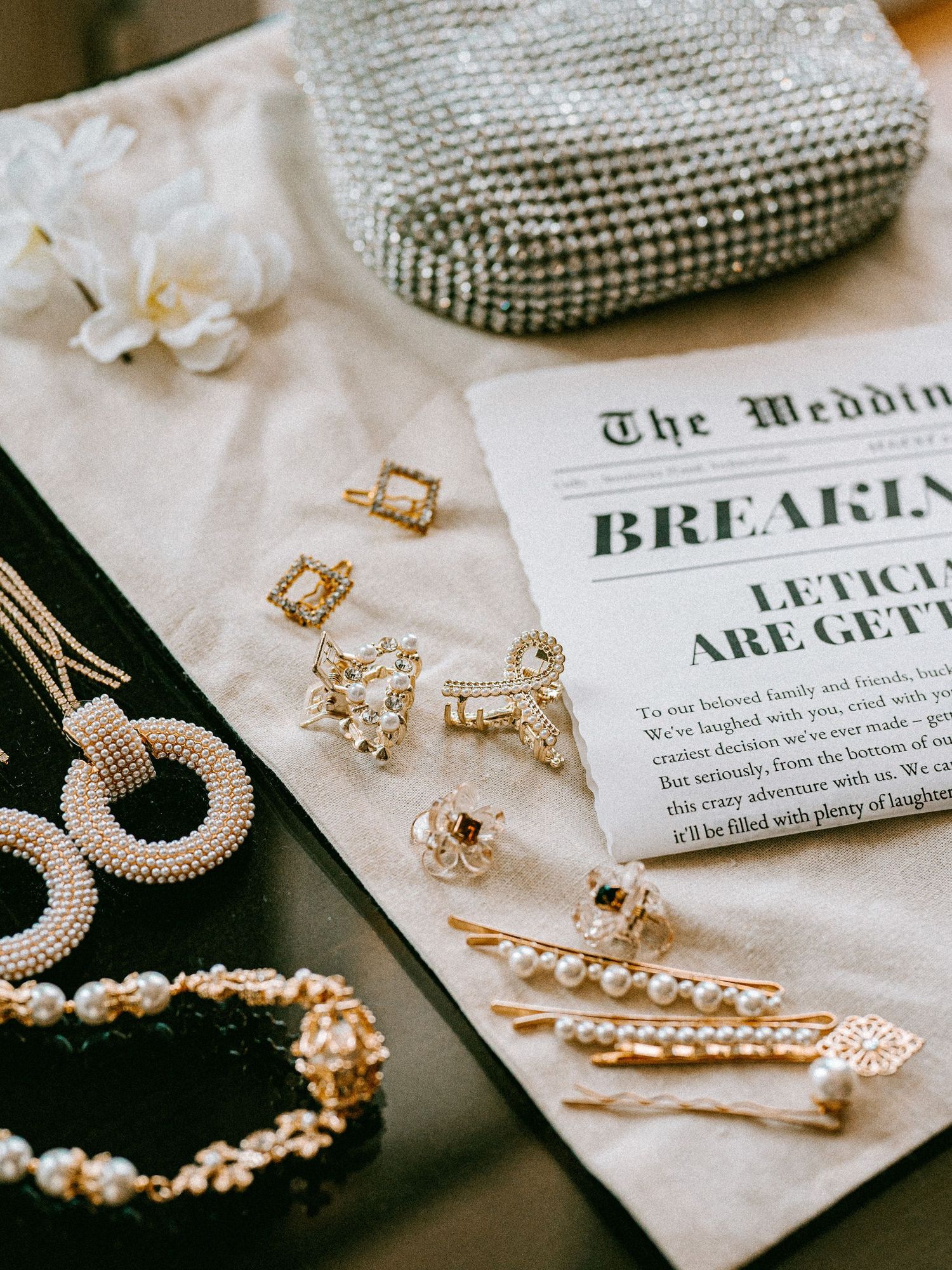 Wedding accessories including jewelry, rings and invitation card arranged on white surface.