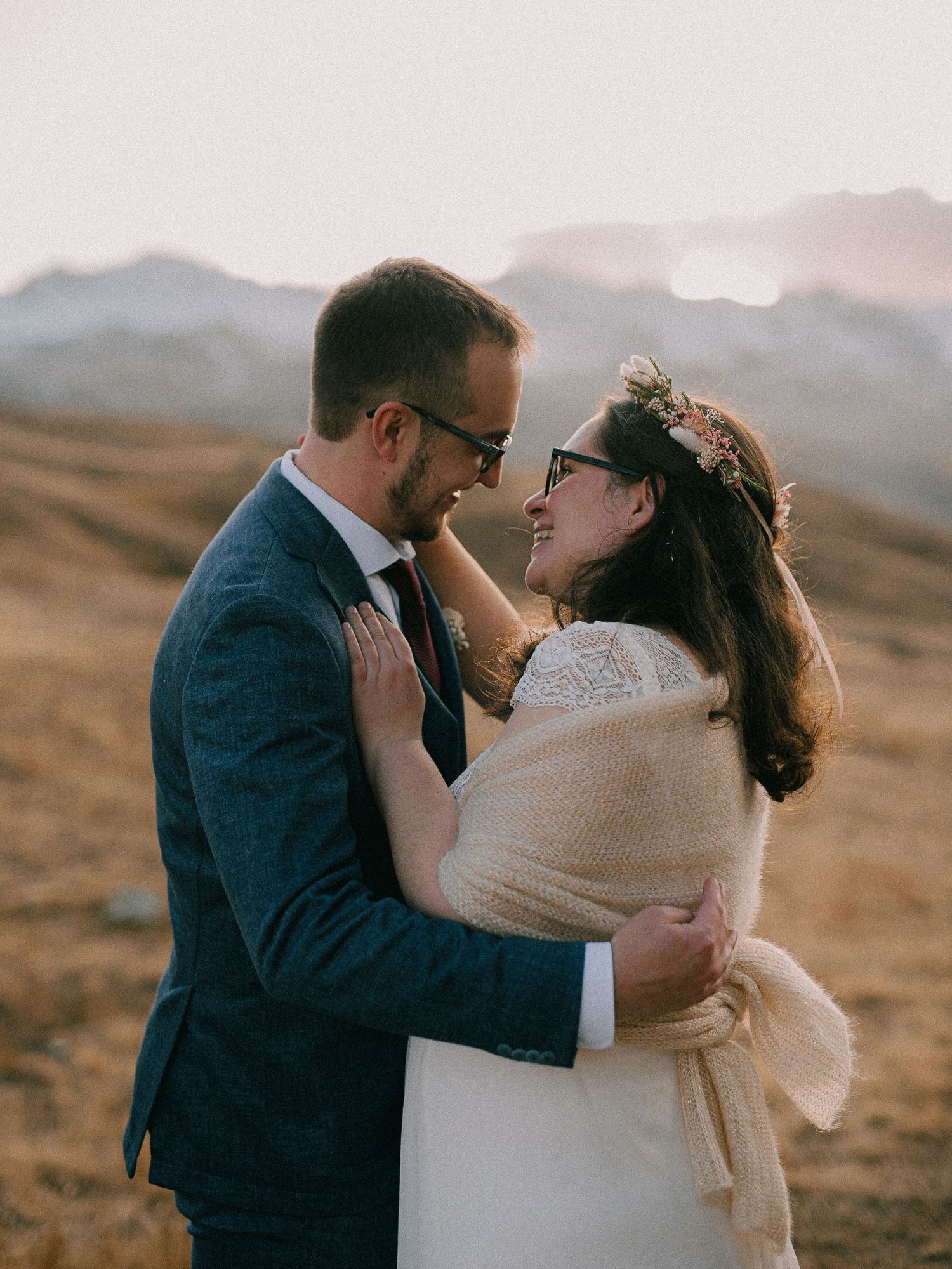A romantic wedding couple shares intimate moments against a mountainous backdrop at sunset.