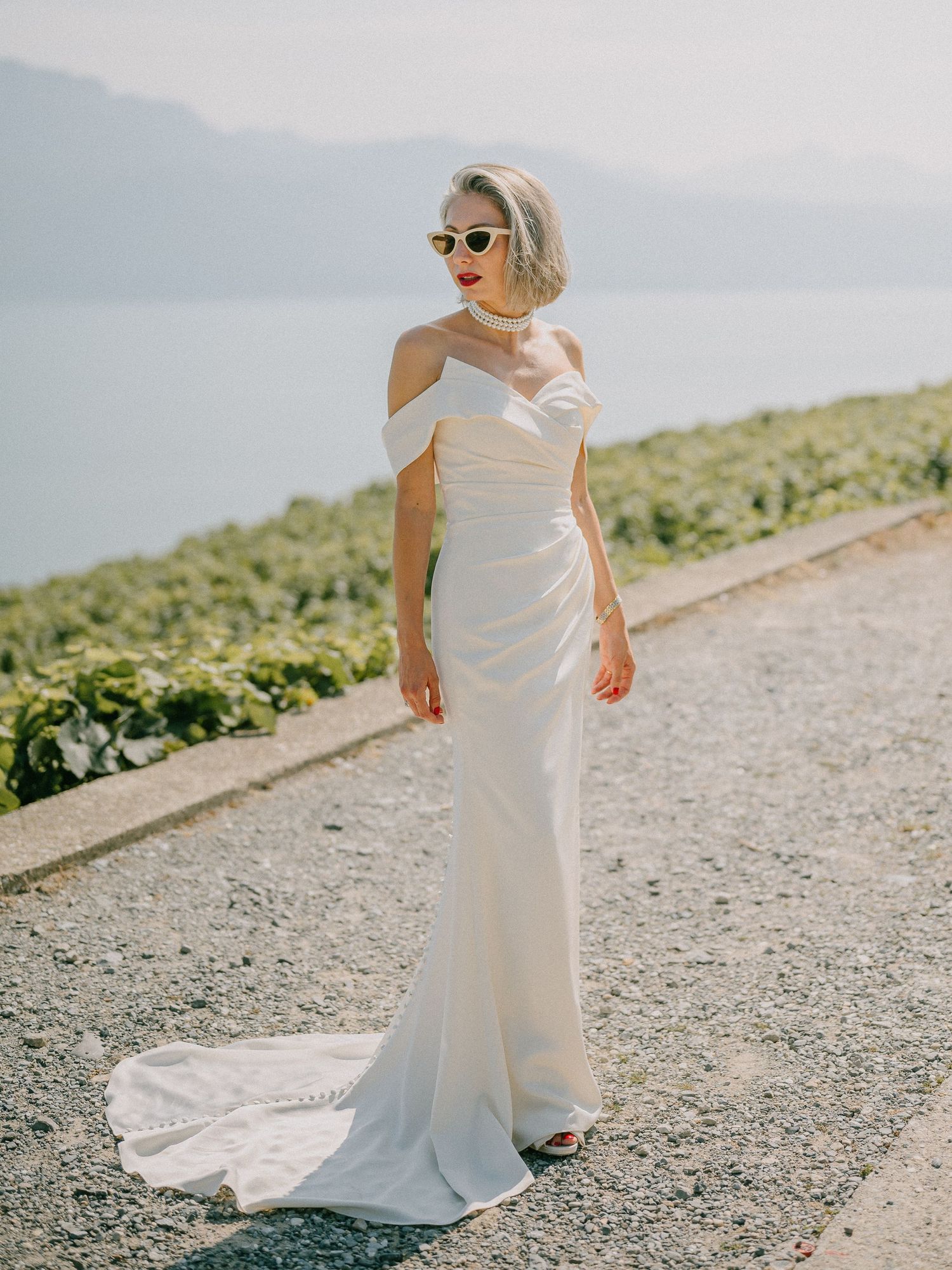 Elegant white wedding dress with off-shoulder design photographed against mountain landscape.