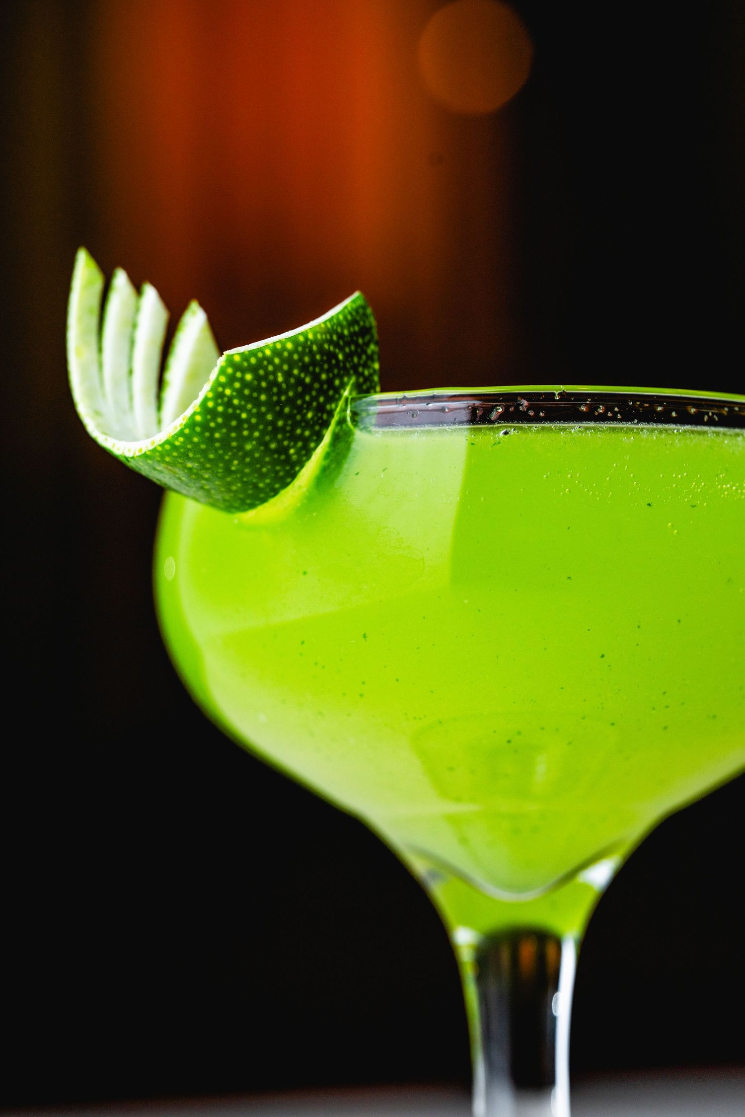 Bright green cocktail in martini glass garnished with fresh lime wheel.
