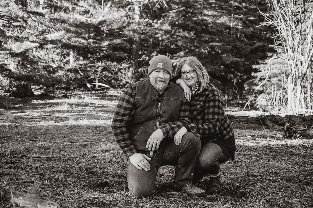 Two people in plaid shirts kneeling outdoors in a winter setting.