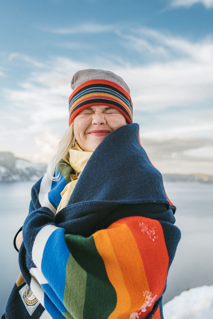 Bundled in a colorful striped blanket against snowy mountain backdrop on a sunny winter day.
