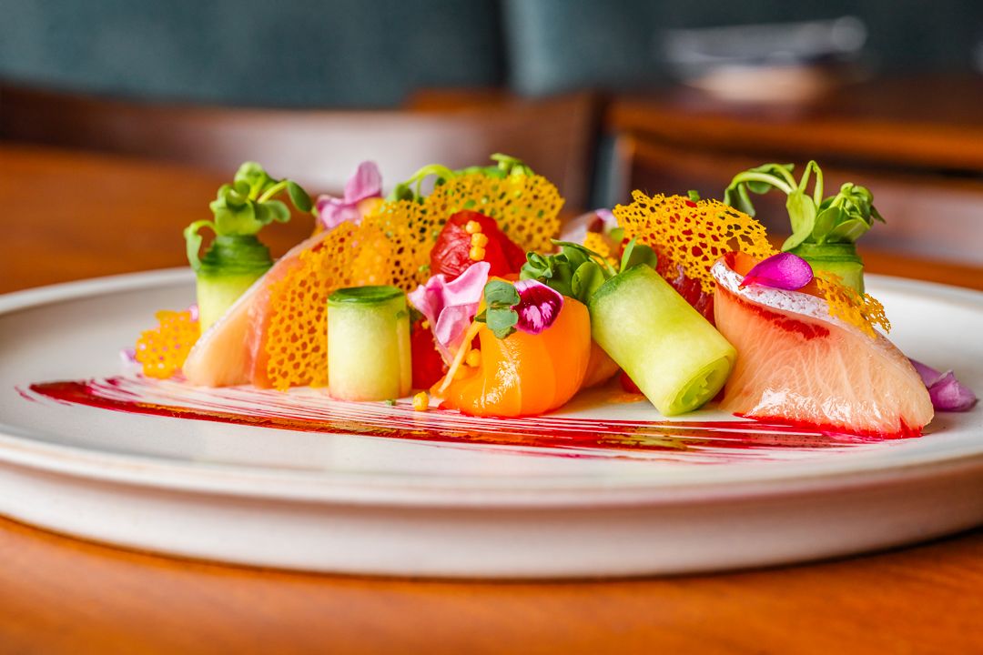 Colorful citrus and seafood dish with microgreens and edible flowers on white plate.
