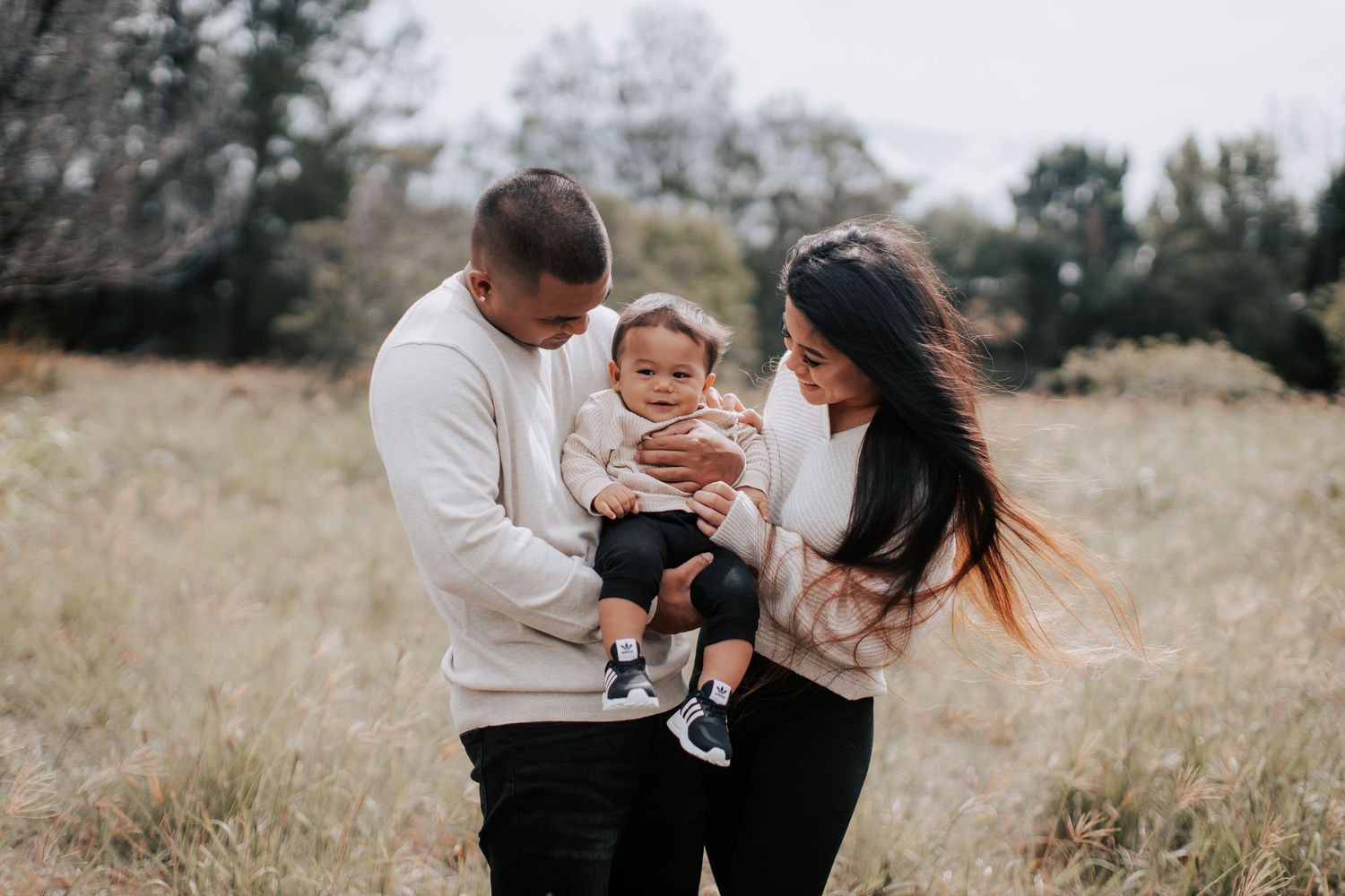 A young family with a baby enjoys an outdoor photo session in a grassy field during autumn.
