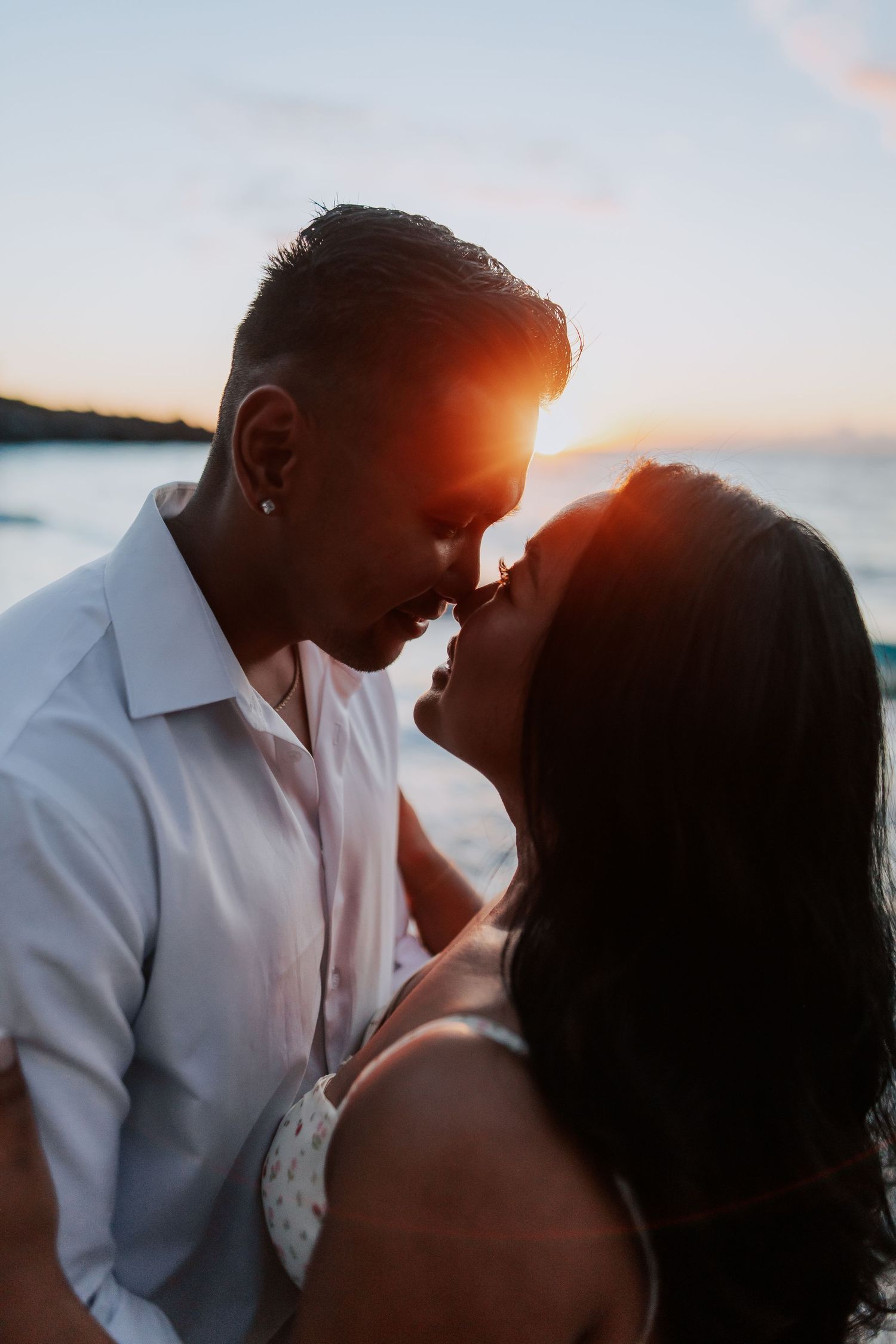 Romantic couple sharing an intimate moment at sunset by the ocean, bathed in warm golden light.