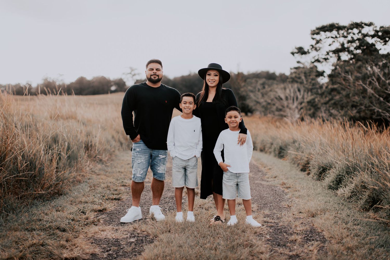 Family of four posing on a dirt path surrounded by golden grass fields during a outdoor photo session.