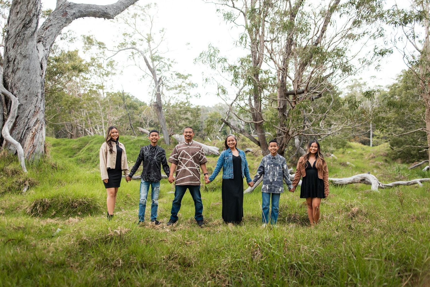 Six people holding hands in a lush green Australian bushland setting with gum trees.