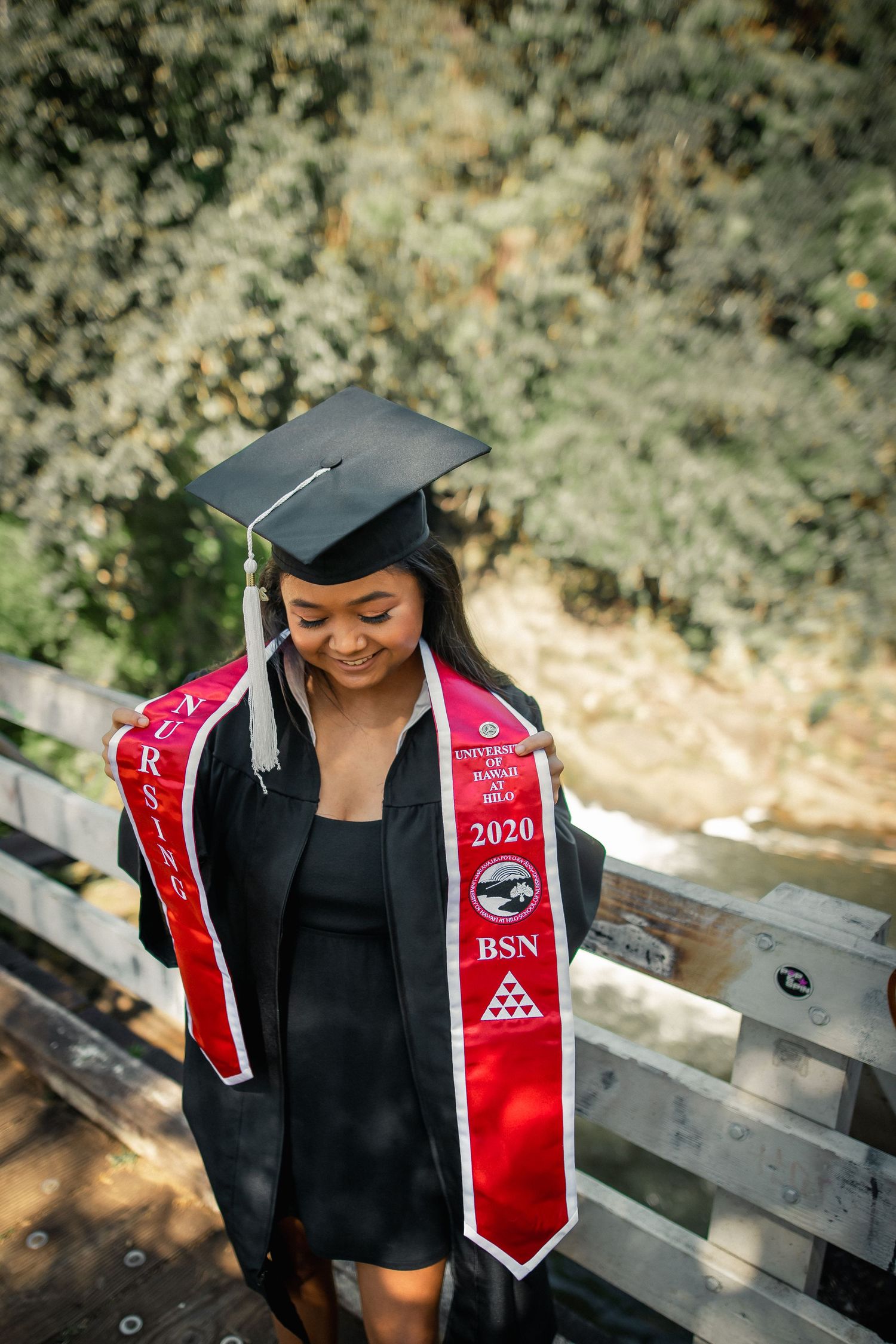A young woman in black graduation gown and cap wearing a red 2020 BSN nursing stole, smiling outdoors.