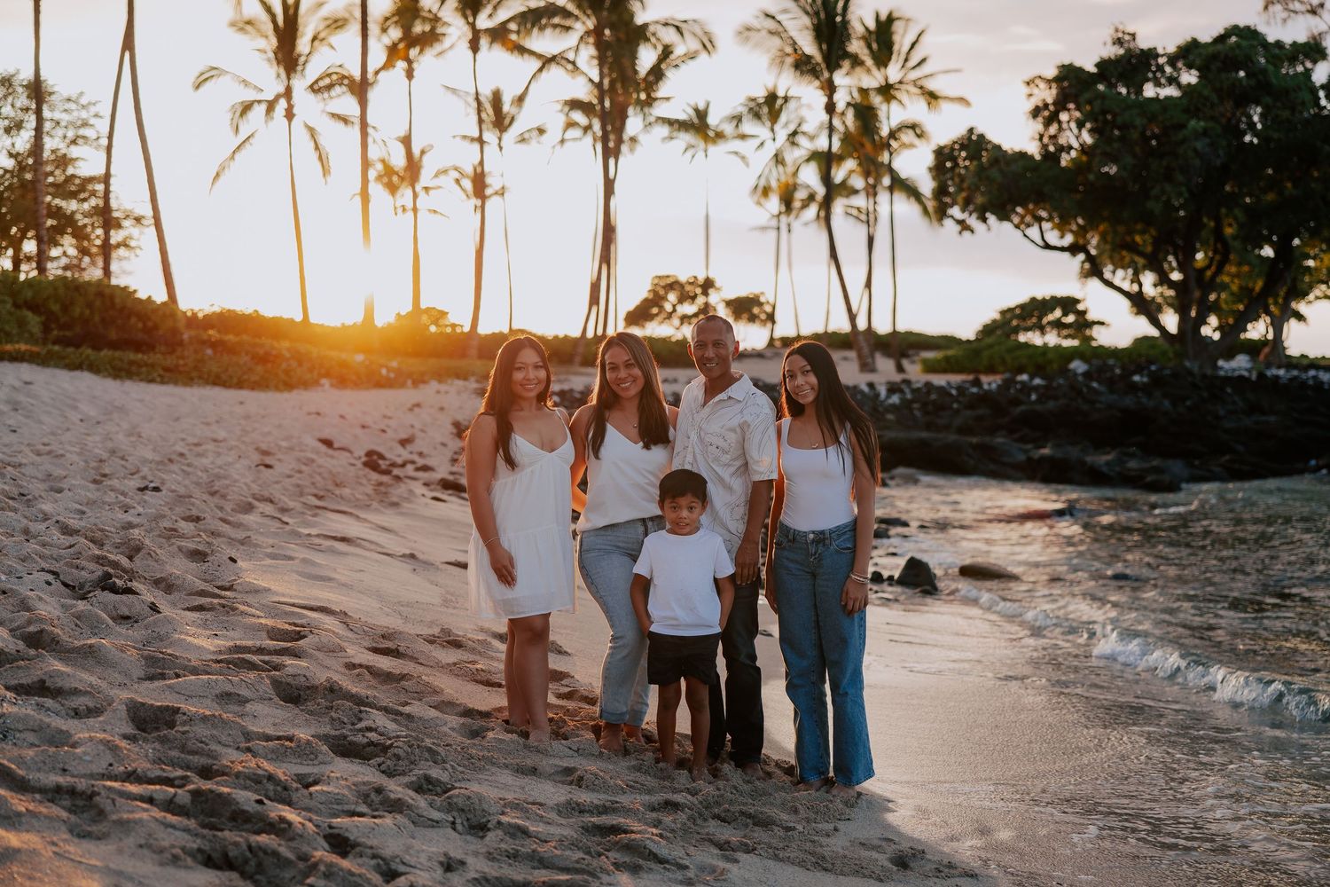 Family of six posing on a sandy beach at golden sunset with tall palm trees in Hawaii.