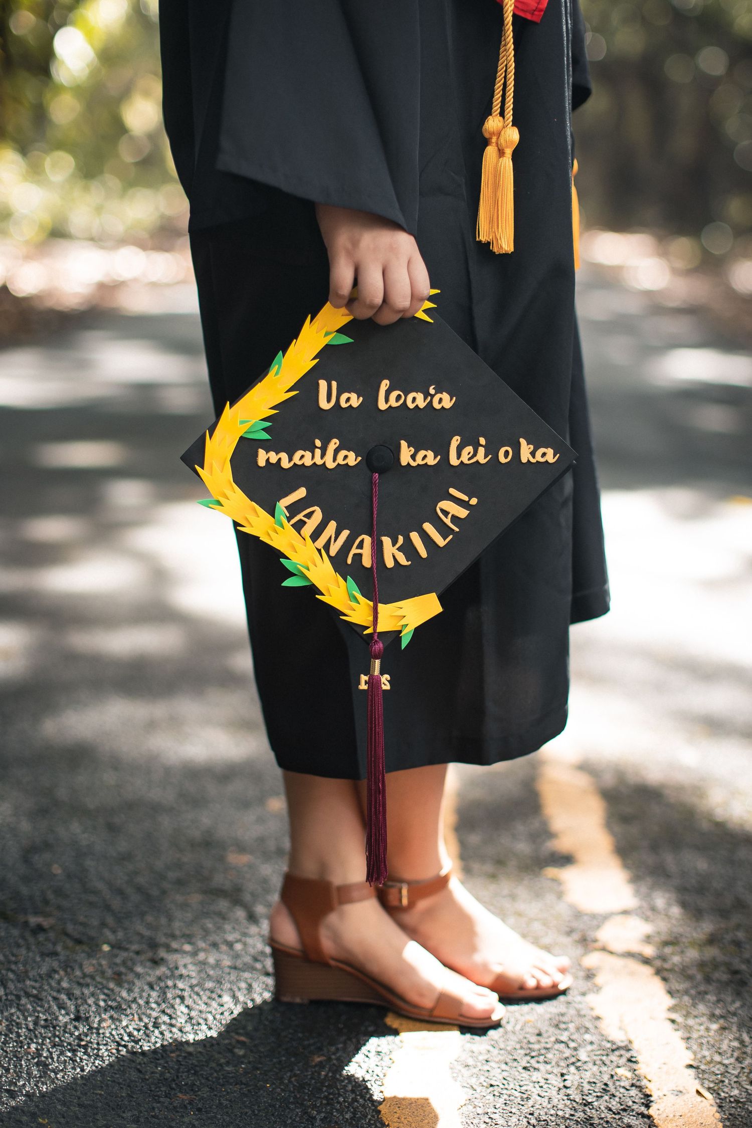 Graduate holding decorated mortarboard cap with Hawaiian phrase 