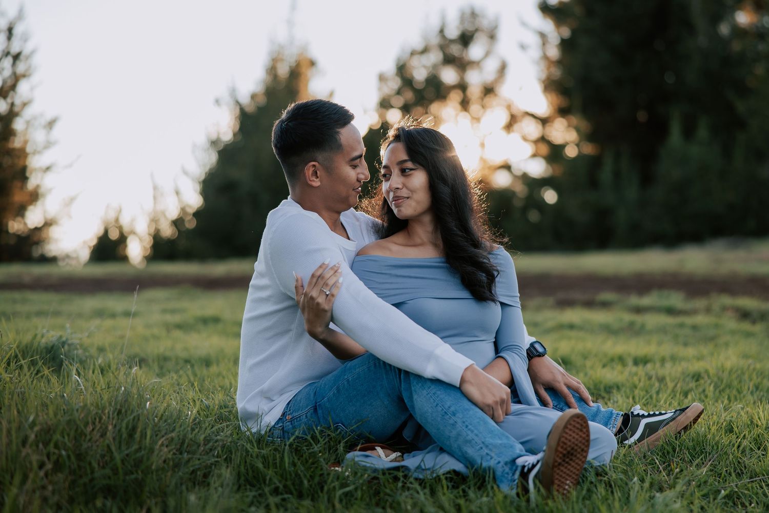 Couple sitting together in a grassy field at sunset, sharing a romantic moment outdoors.