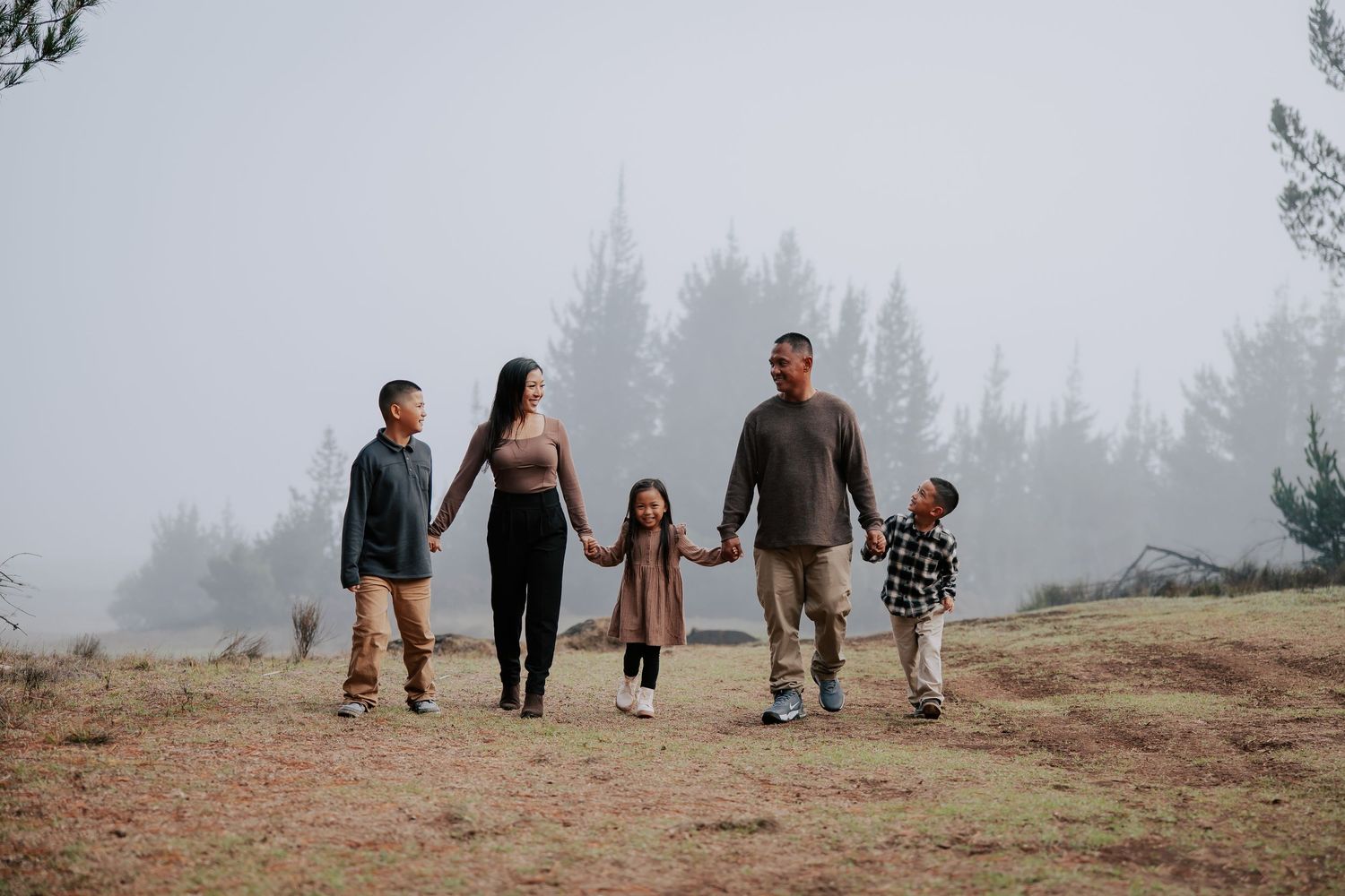 Family of five holding hands walking through a misty forest clearing on a foggy day.