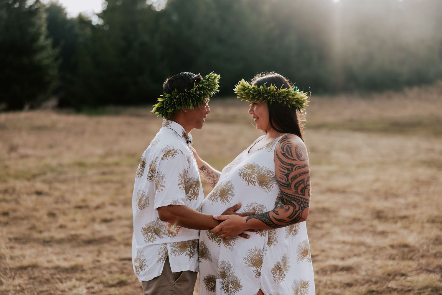 Couple in matching floral outfits and leaf crowns hold hands in a sunlit field.
