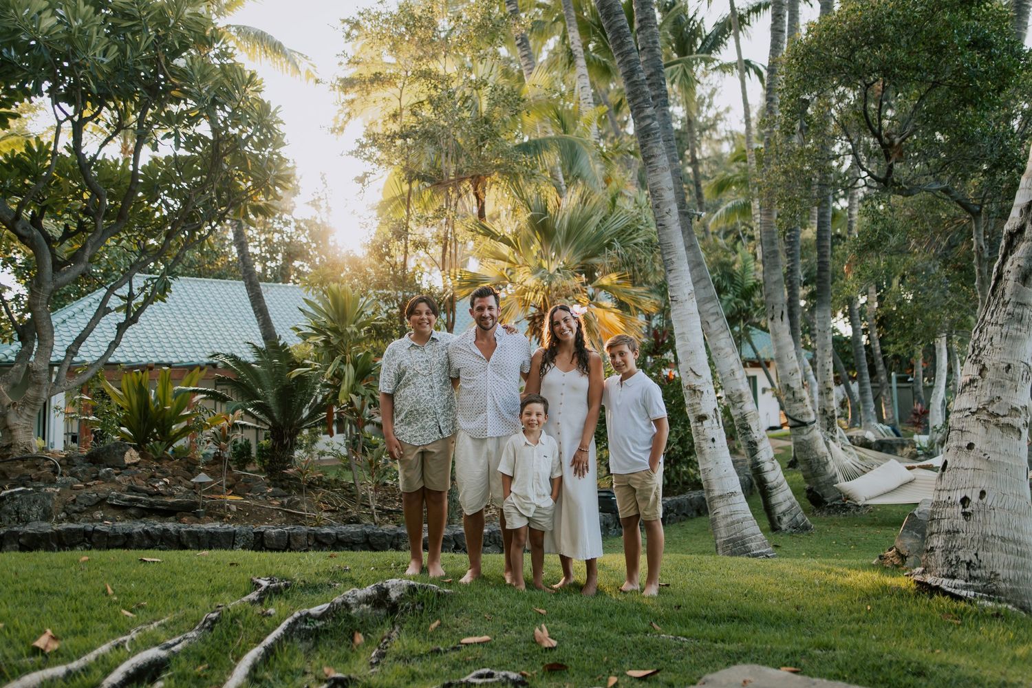 Family of six posing together on lush tropical resort grounds surrounded by palm trees and golden sunlight.