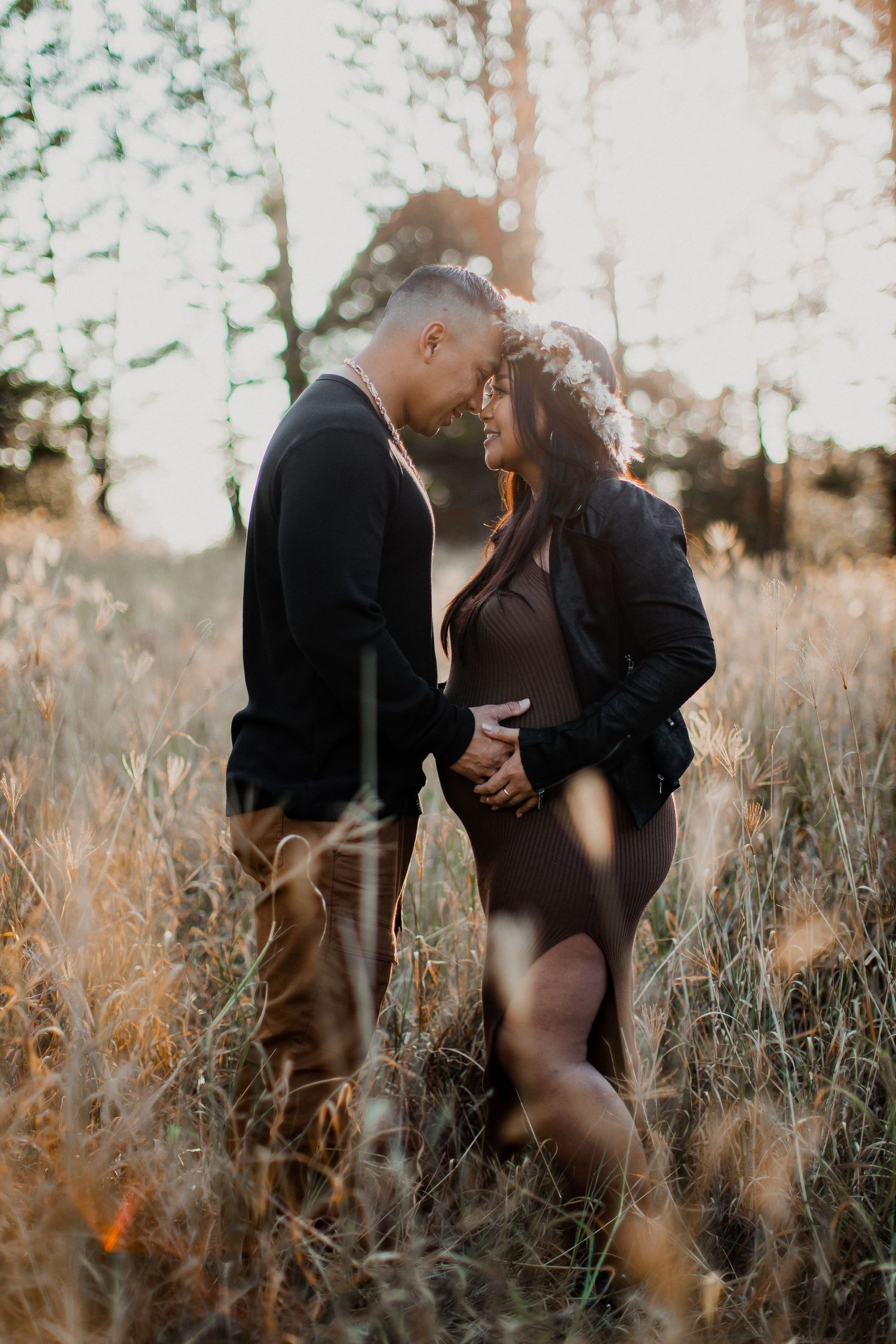 Couple sharing a tender moment in a golden sunlit field, holding hands and touching foreheads at sunset.