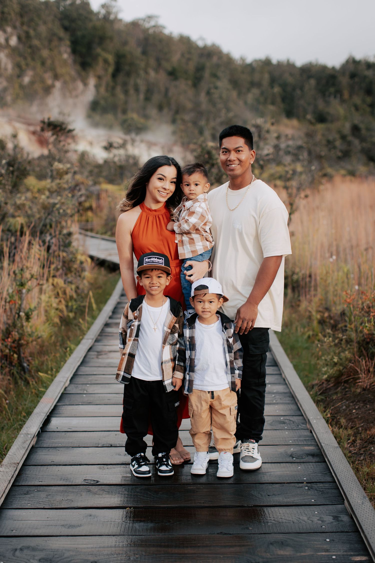 Family of five posing on a wooden boardwalk surrounded by lush greenery and misty hills.