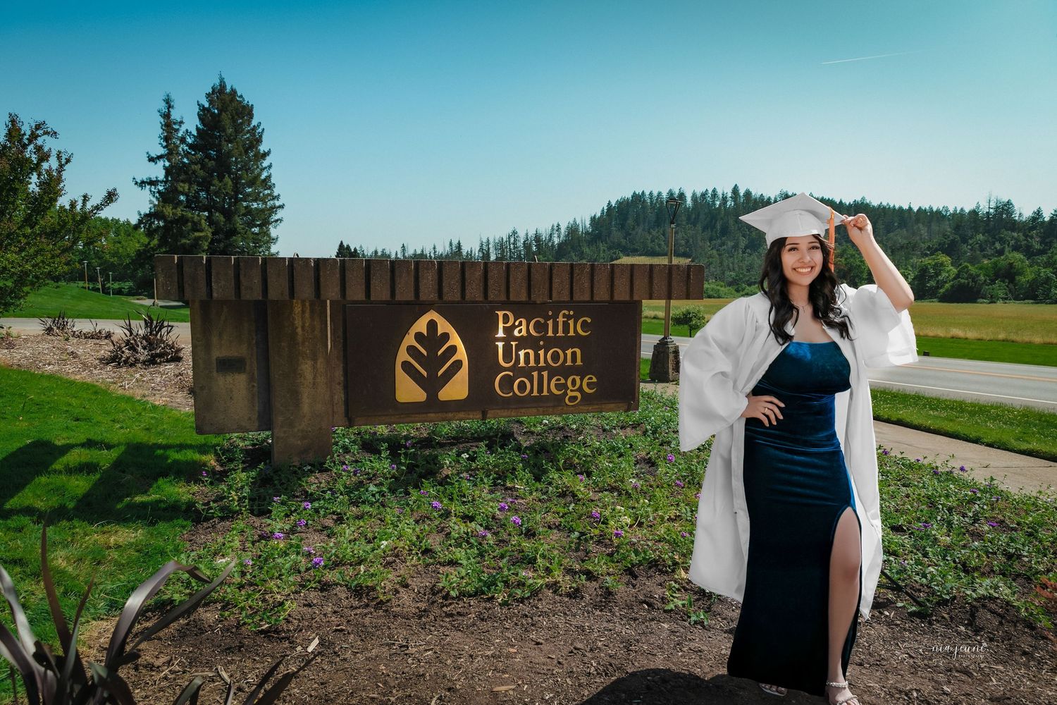 Graduate poses with white hat at Pacific Union College entrance sign.