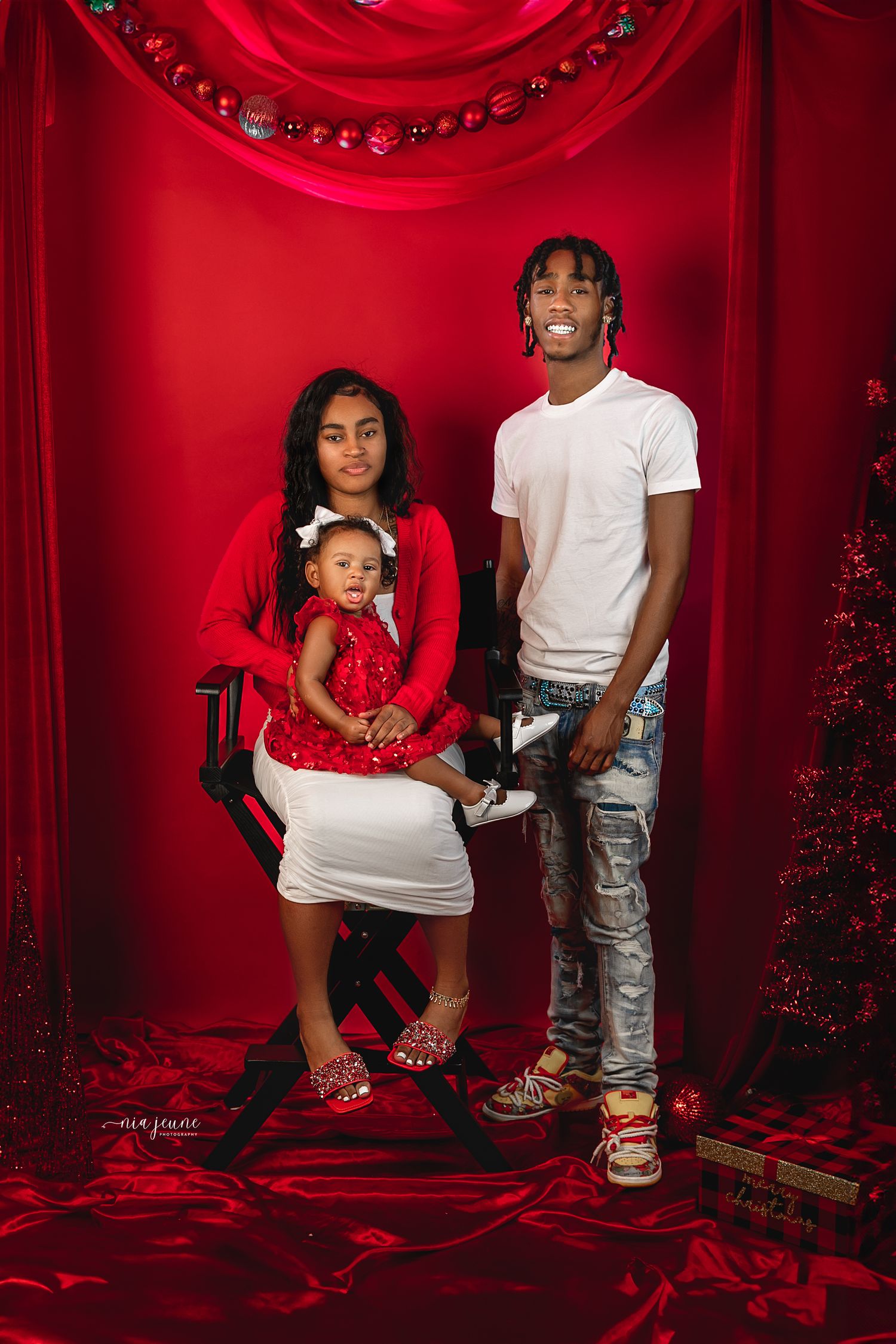 Family Christmas portraits with red backdrop and festive holiday decorations.