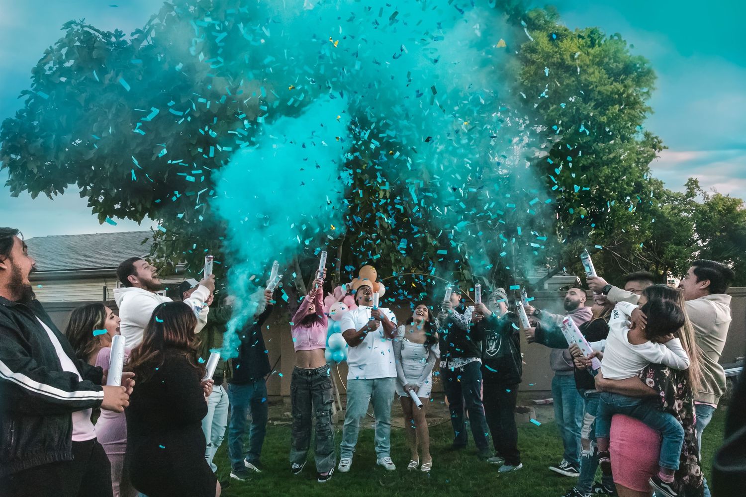 A group gathers outdoors for a festive gender reveal party as blue powder explodes in celebration.