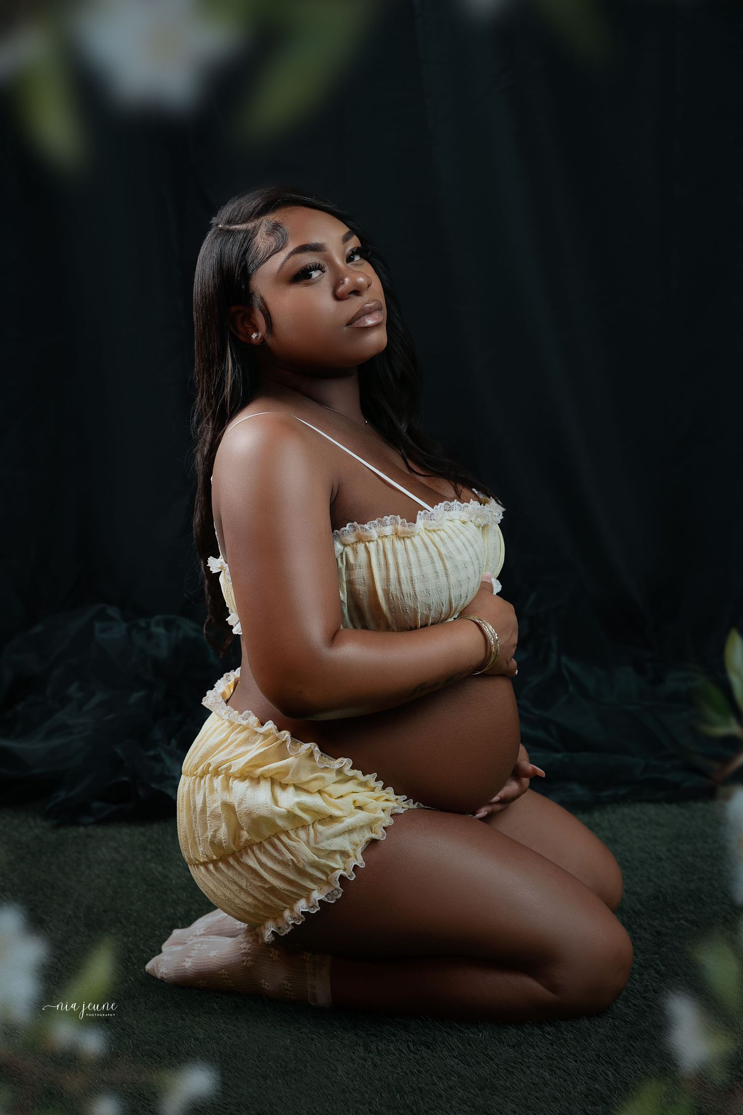 Artistic maternity photoshoot featuring an expecting mother in a yellow ruffled dress against a dark background.