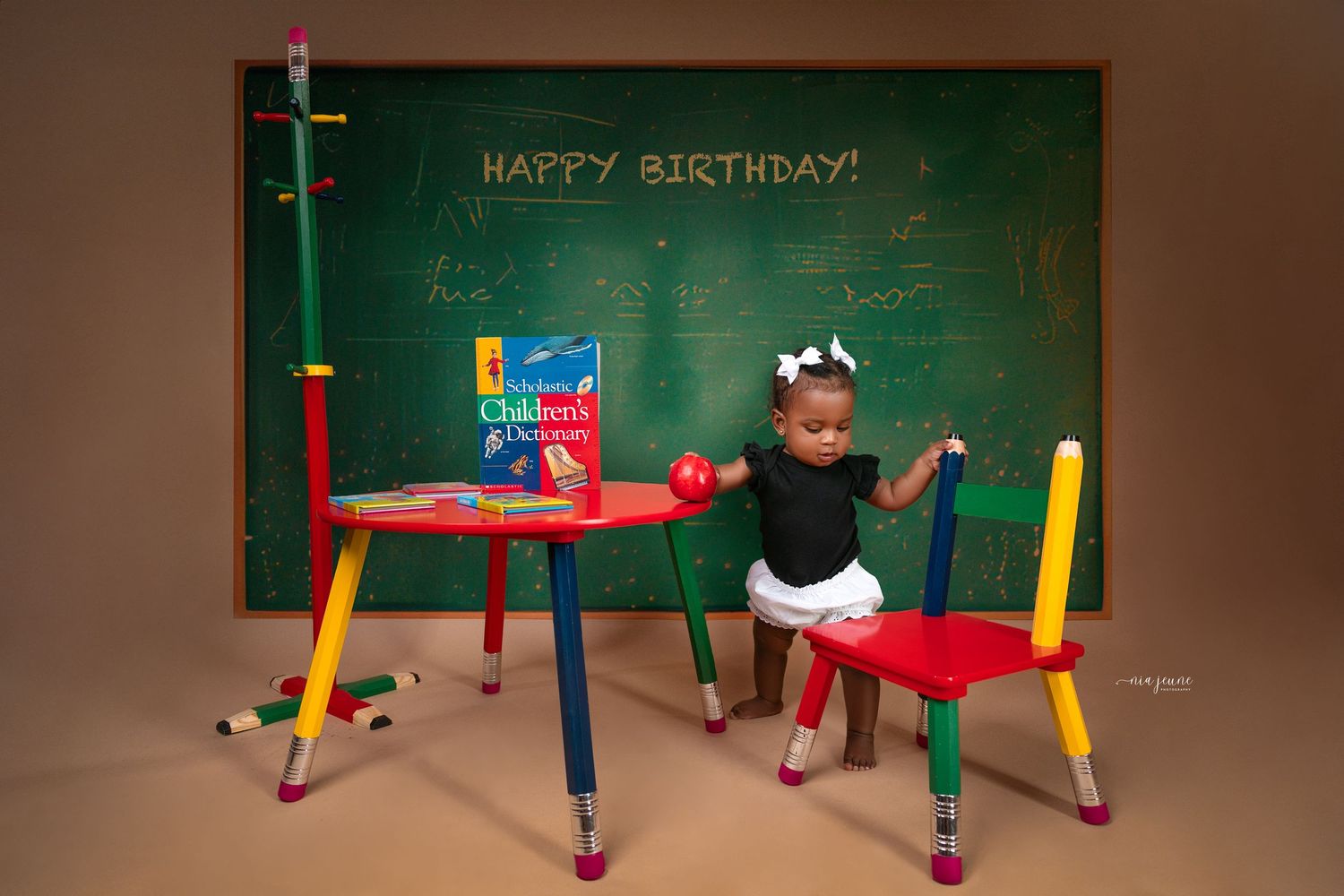 Birthday-themed photo setup with colorful chairs and chalkboard displaying birthday message.
