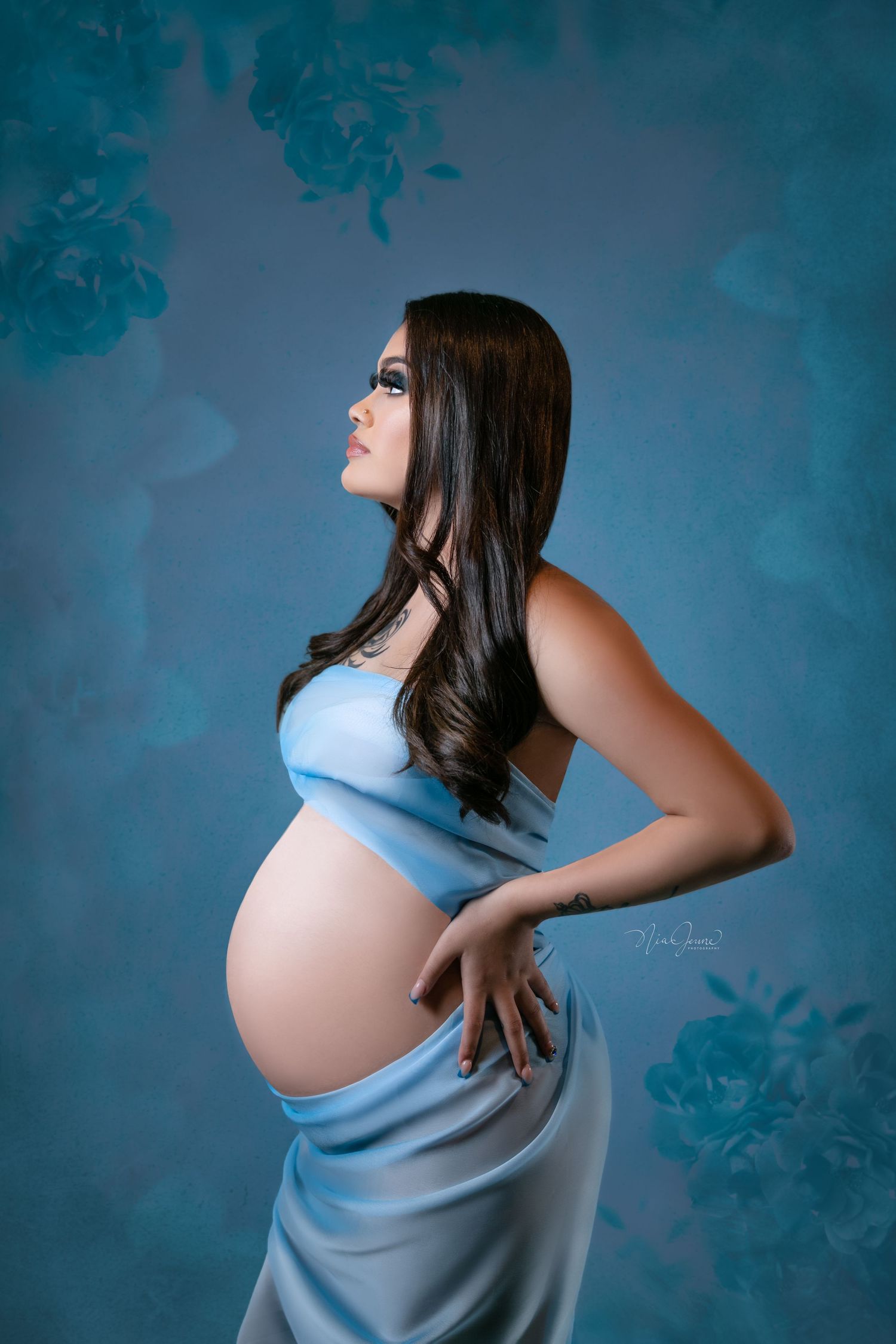 Artistic maternity photo with blue dress against floral backdrop.