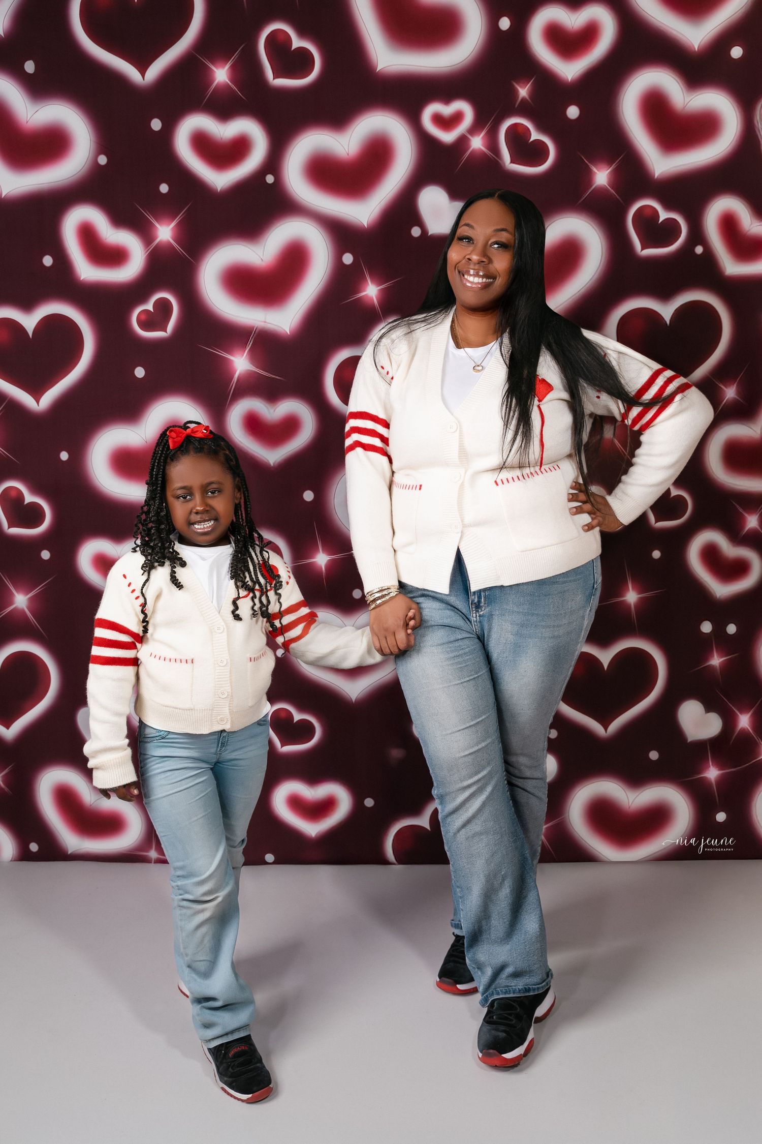 Valentine's themed photo shoot against heart pattern backdrop with casual white and denim outfits.