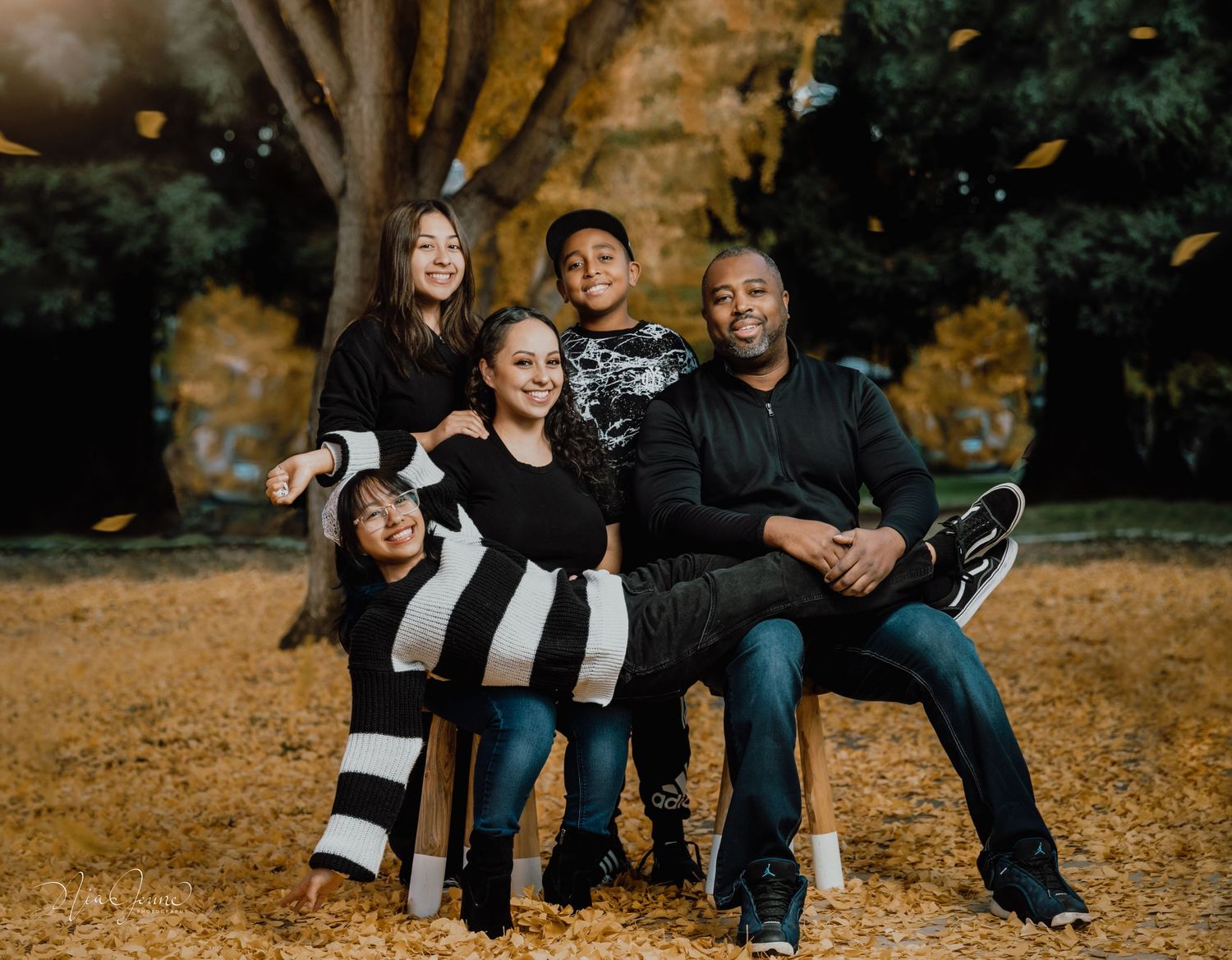 Family sitting together on fallen autumn leaves in a park during golden hour sunset.