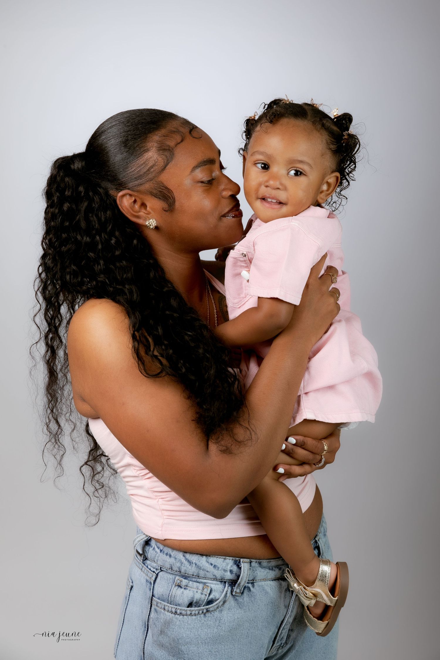 A tender moment captured between a parent and child in matching pink outfits against a grey studio backdrop.
