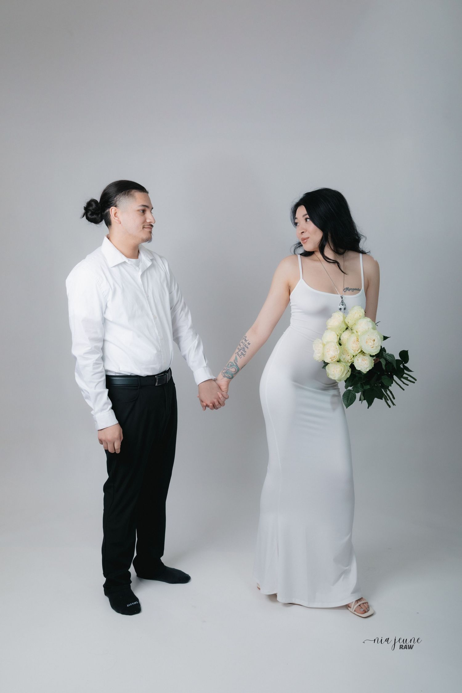 Minimalist wedding portrait with couple holding hands against white backdrop with yellow roses.