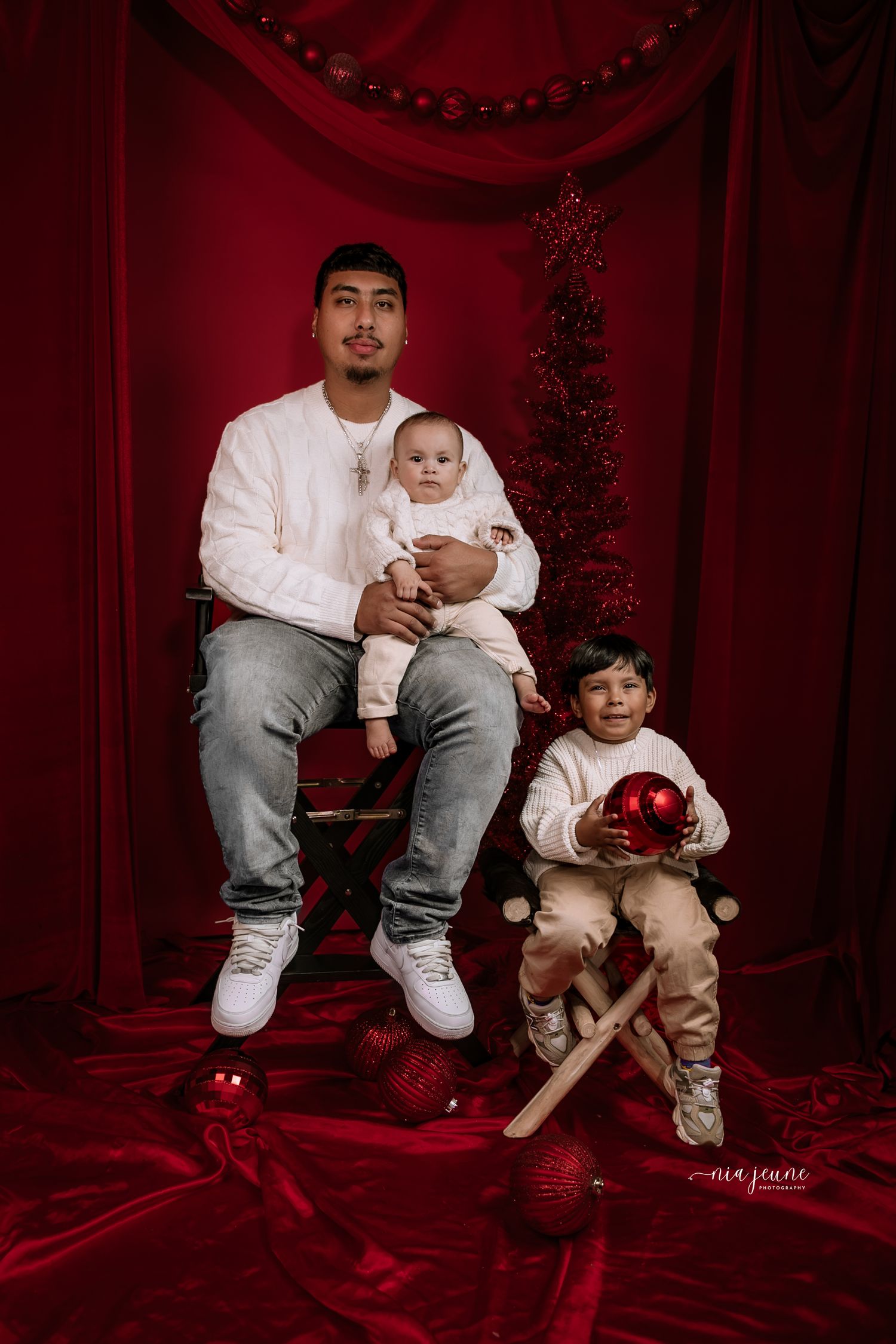 Children's Christmas portrait session with red ornaments and decorative holiday backdrop.
