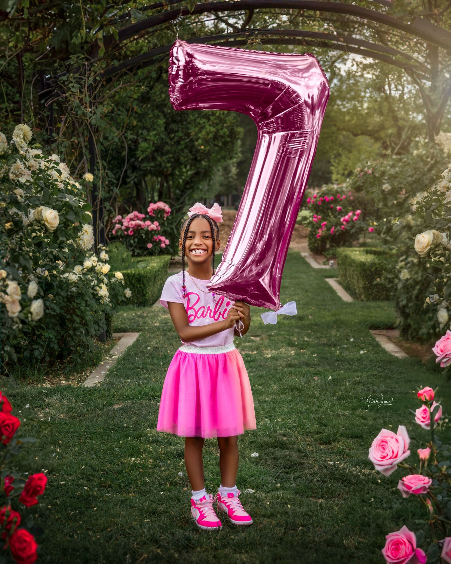 Birthday celebration photoshoot in a rose garden with pink balloon decorations.