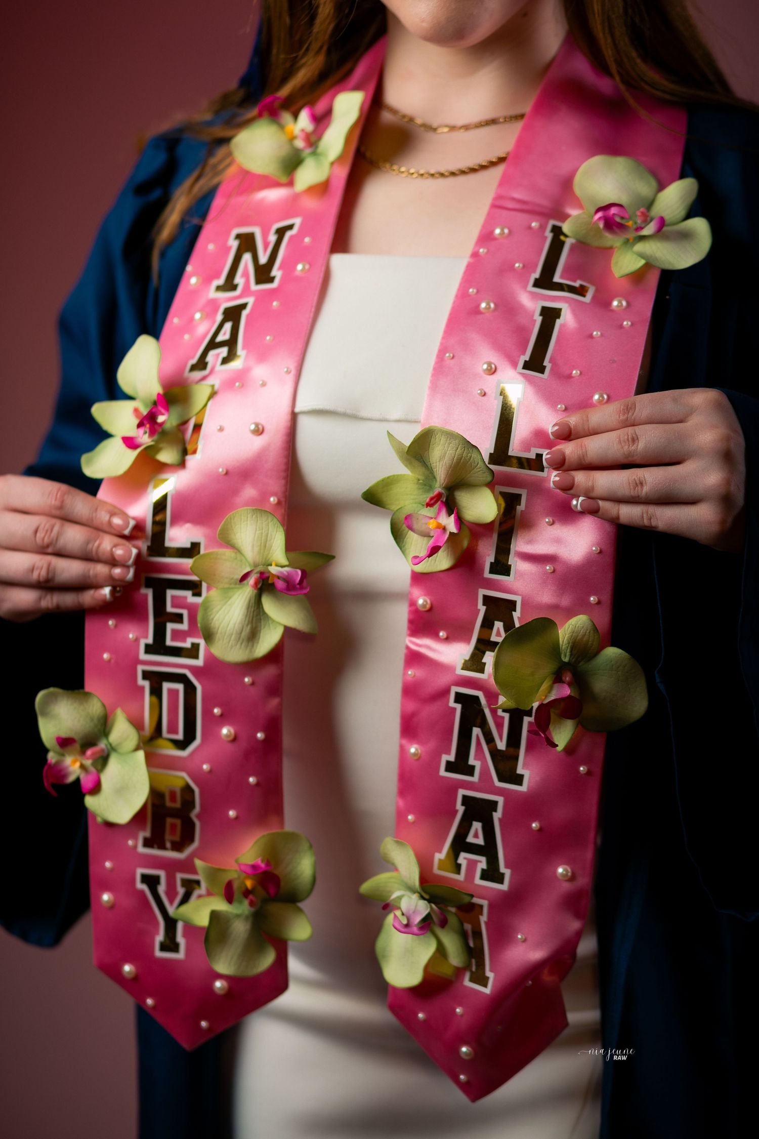 A series of pink graduation stoles adorned with green orchids and embroidered letters, shown in close-up detail shots.