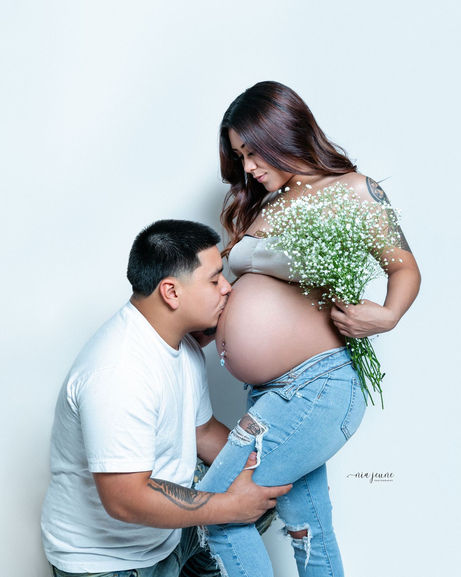 Expectant couple poses with white flowers in intimate maternity photoshoot.
