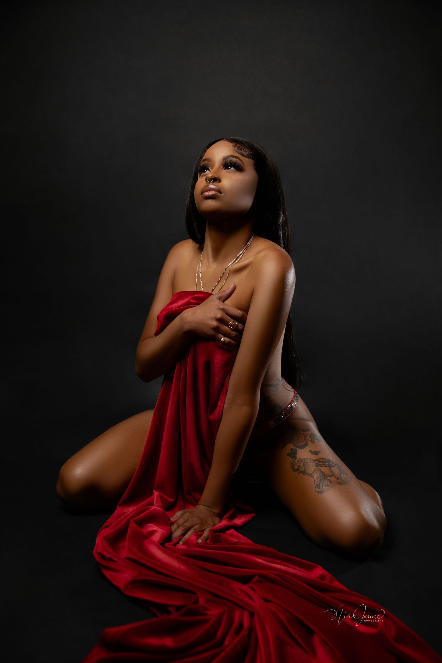 An artistic portrait featuring a person in a flowing red dress fabric against a dark background creating dramatic contrast.
