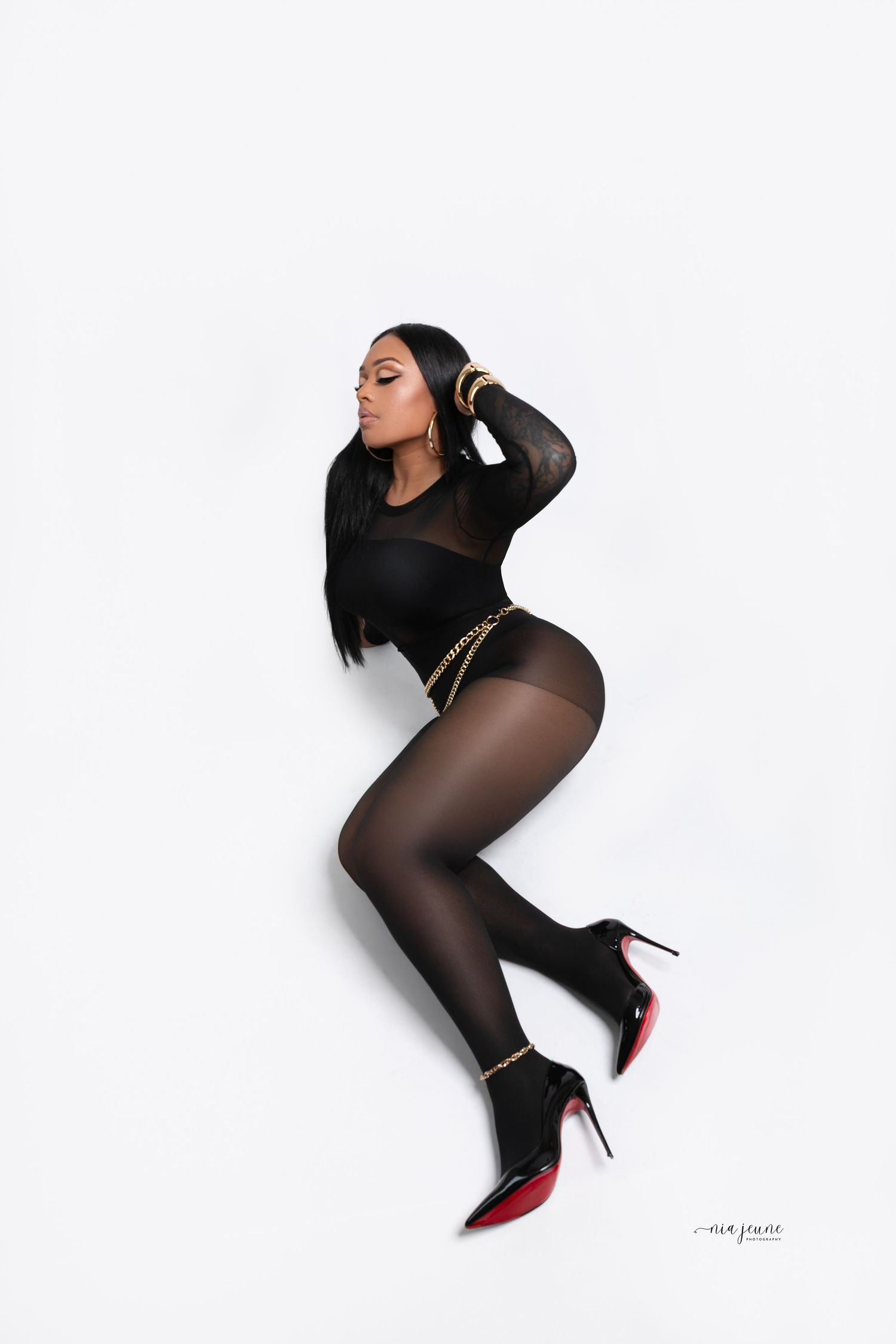 Fashion portrait in black bodysuit and sheer tights against white background.