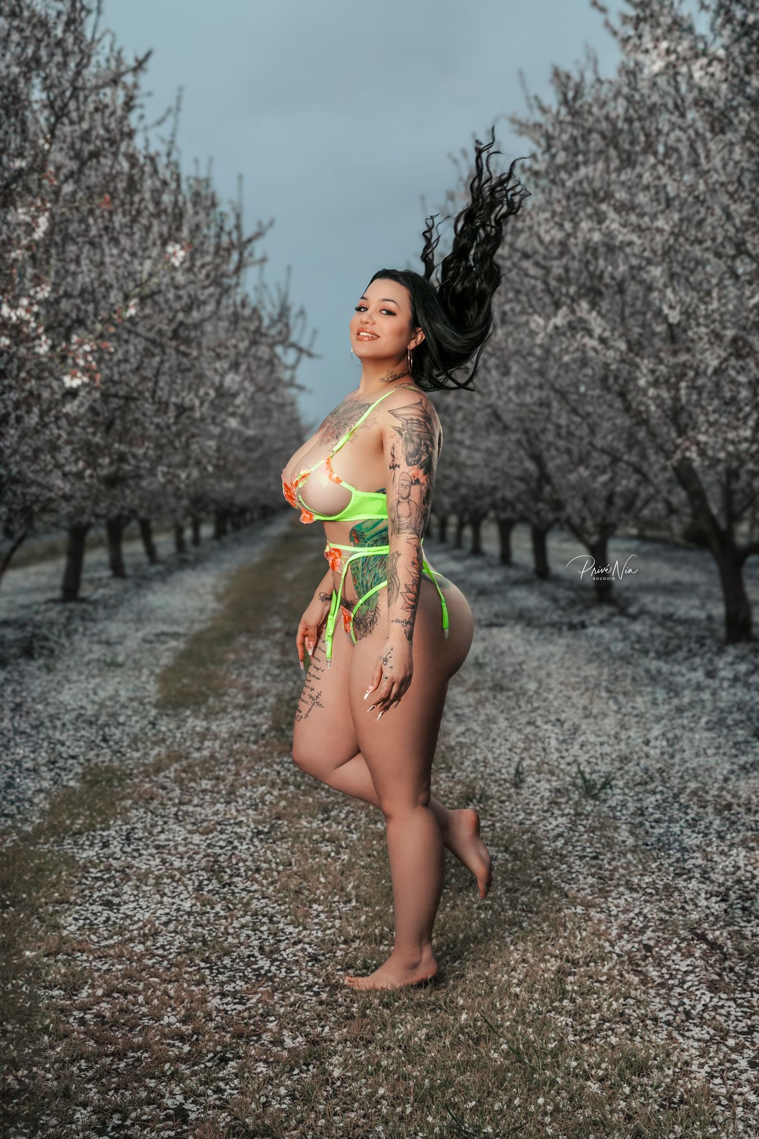 Artistic outdoor portrait in blooming orchard showing person in green swimwear with flowing hair.