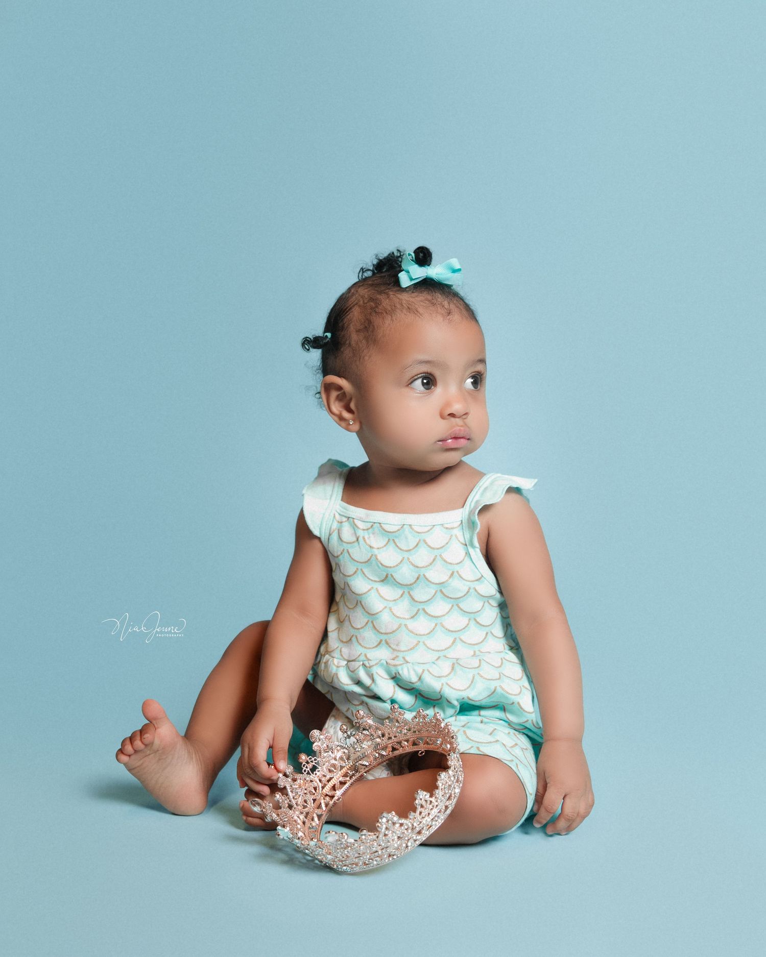 Baby in mint green outfit poses against light blue background for milestone photos.