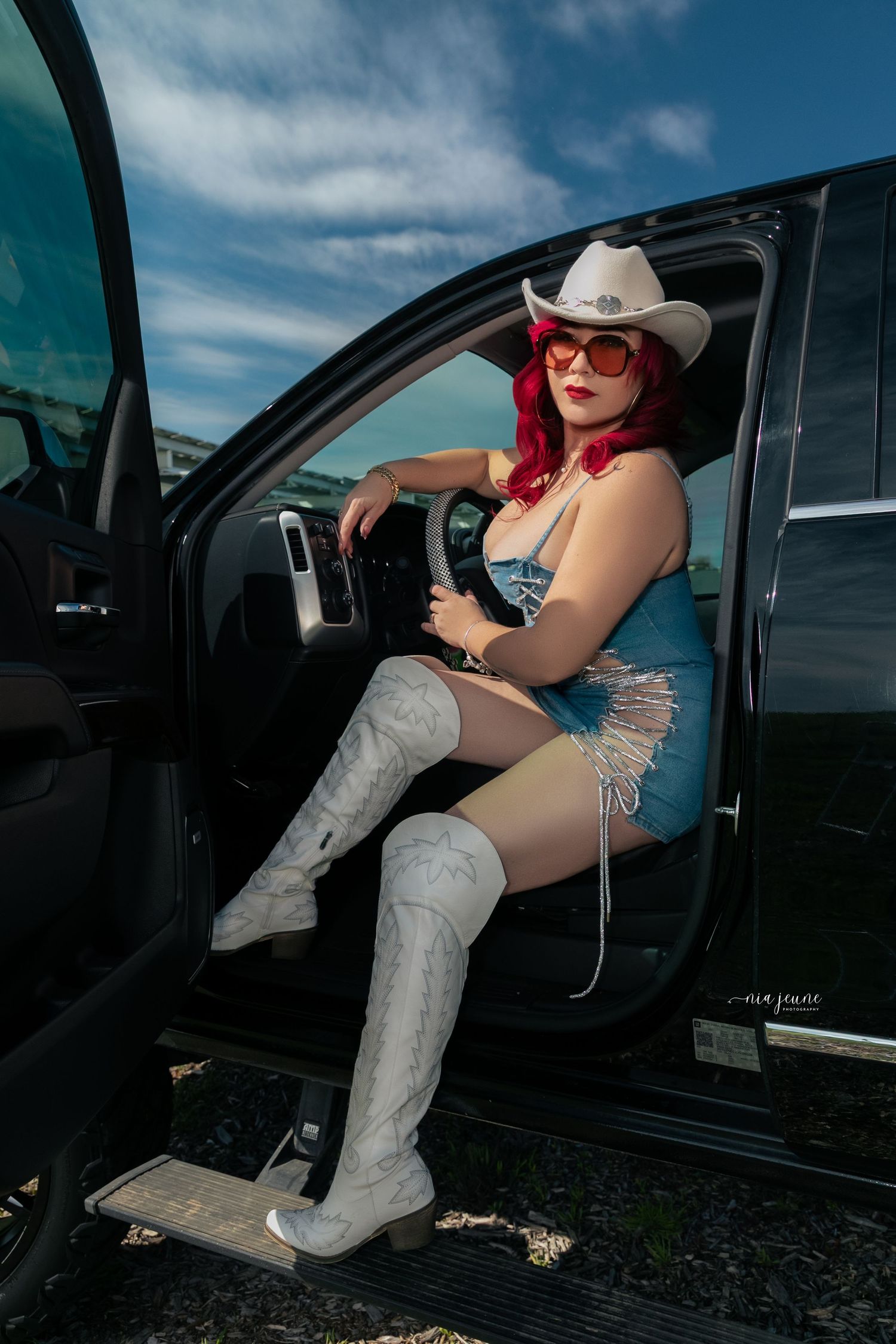 Western-themed portrait in a black vehicle featuring cowboy boots and a white hat.