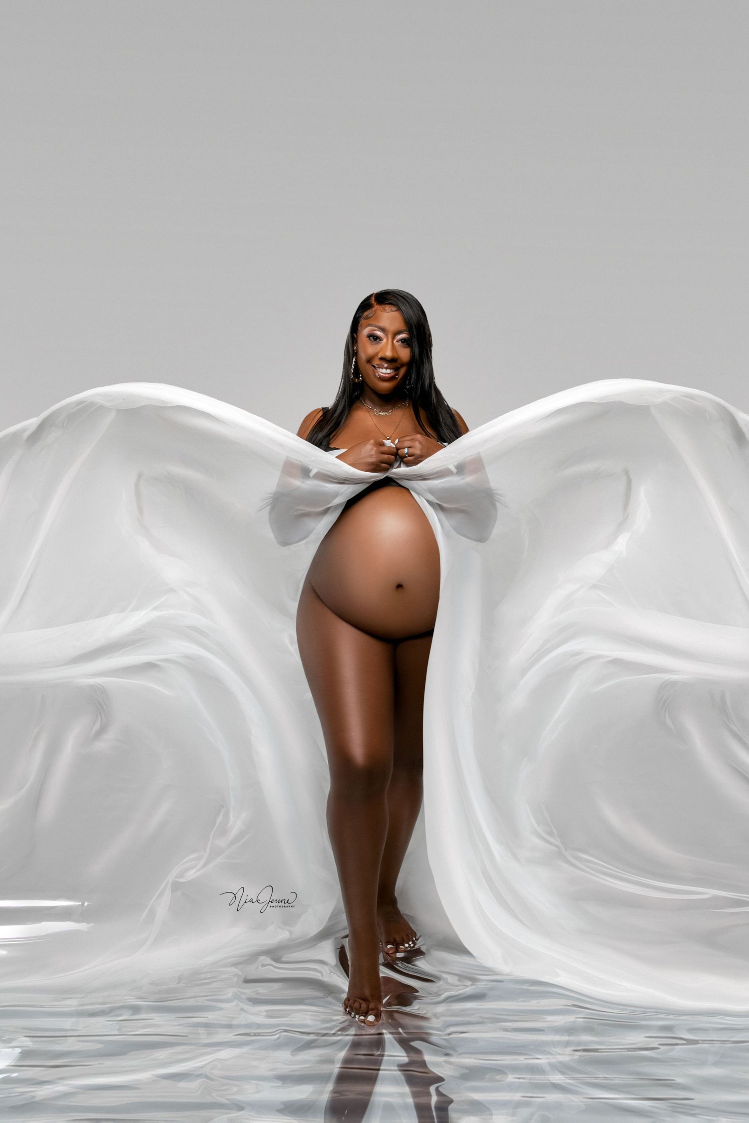 Artistic maternity photo with flowing white fabric against grey background.