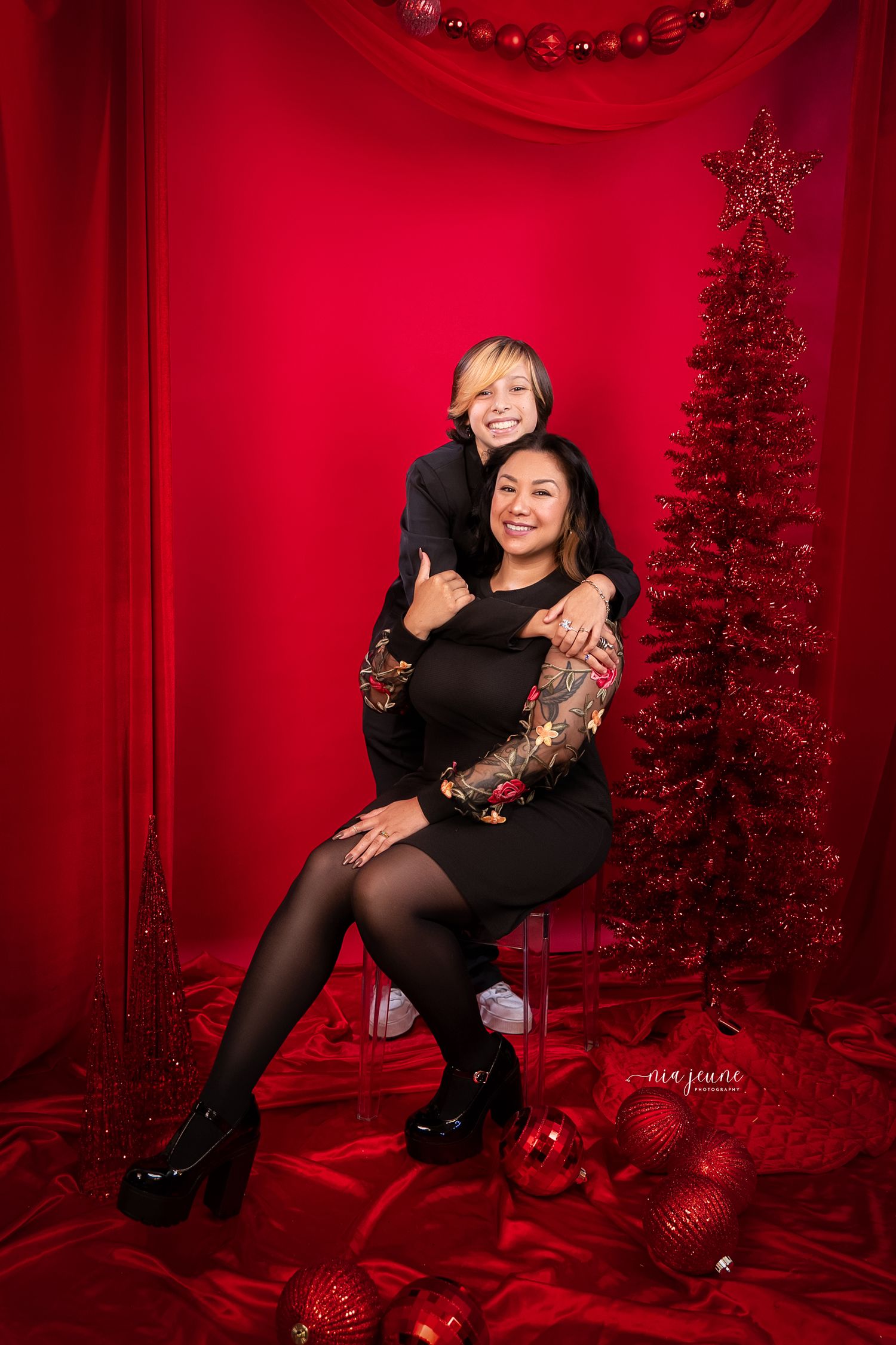 Holiday themed photoshoot with red backdrop and Christmas decorations in studio setting.