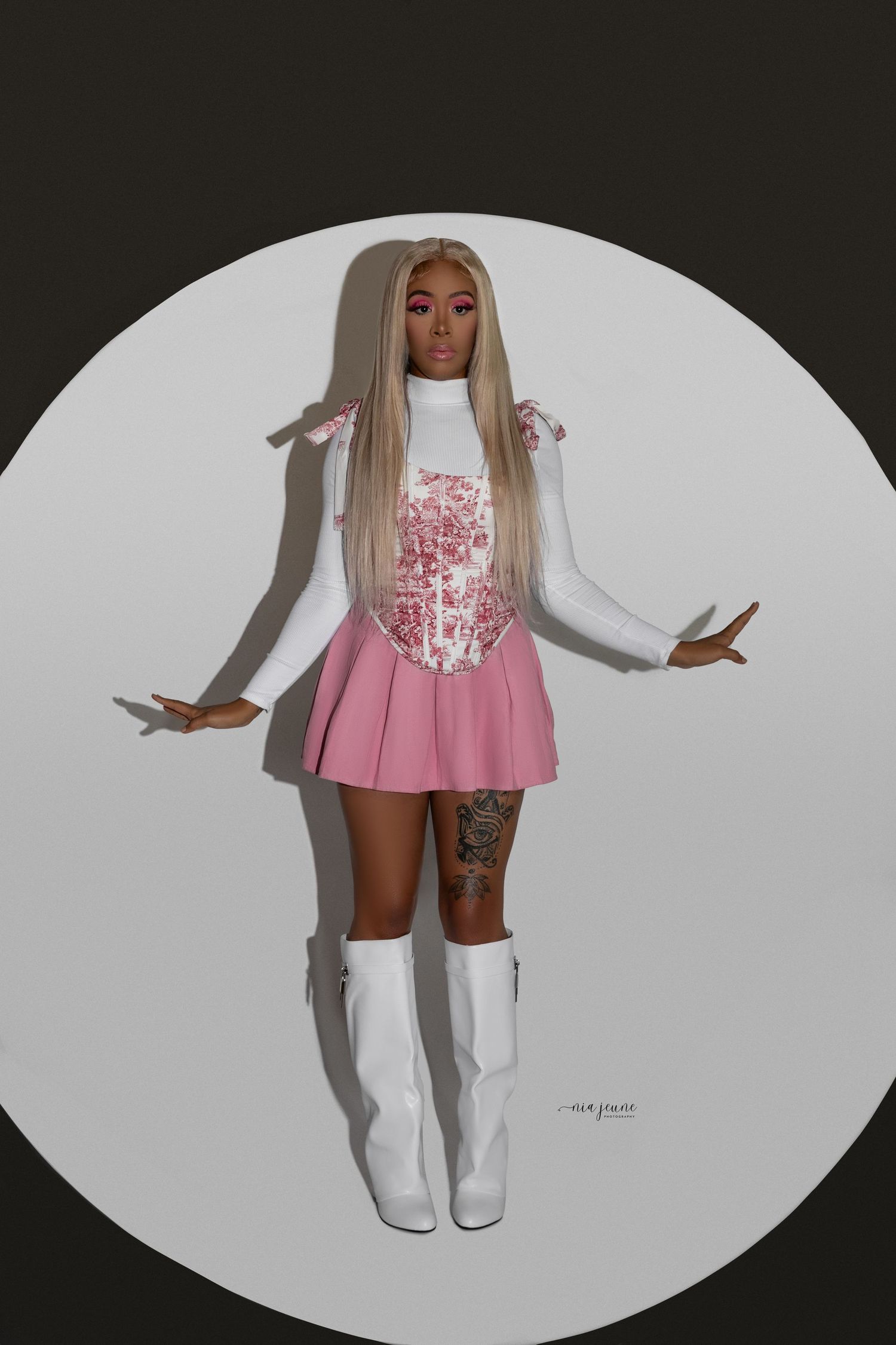 Fashion model in pink and white outfit with long platinum hair posing against circular white backdrop.