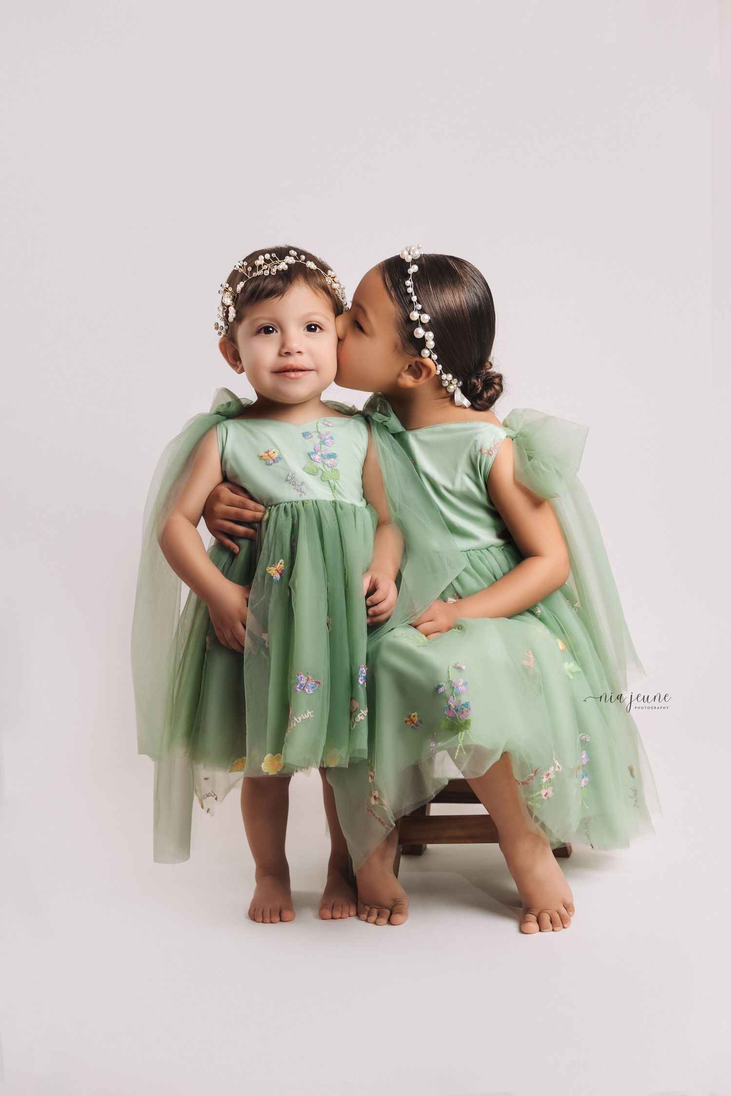 Sweet portrait of two young children in matching mint green dresses with pearl headbands.