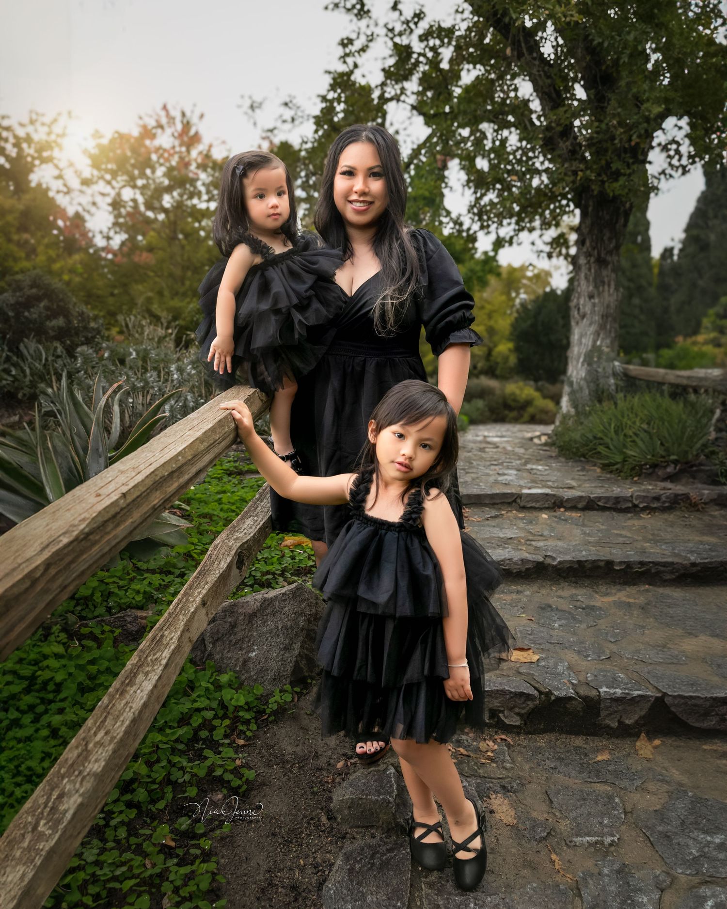 Family photoshoot of mothers and children in black dresses on rustic outdoor stone steps.