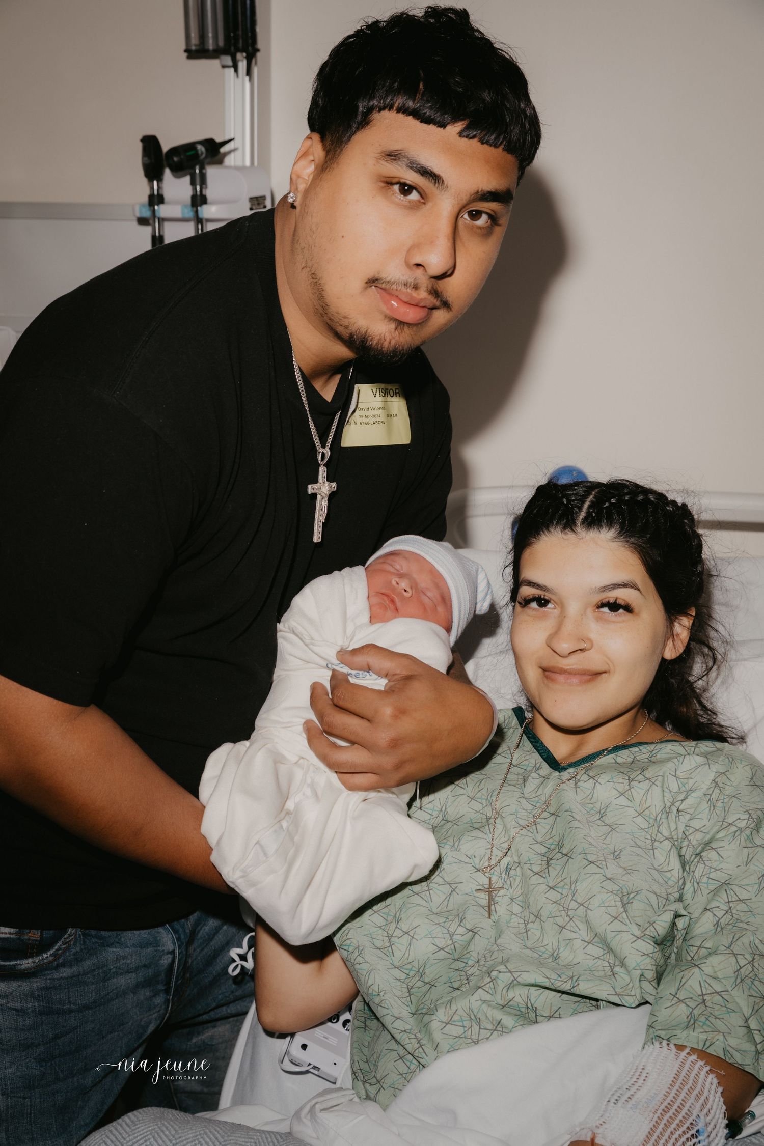 New parents with newborn baby in hospital room share intimate moment together.