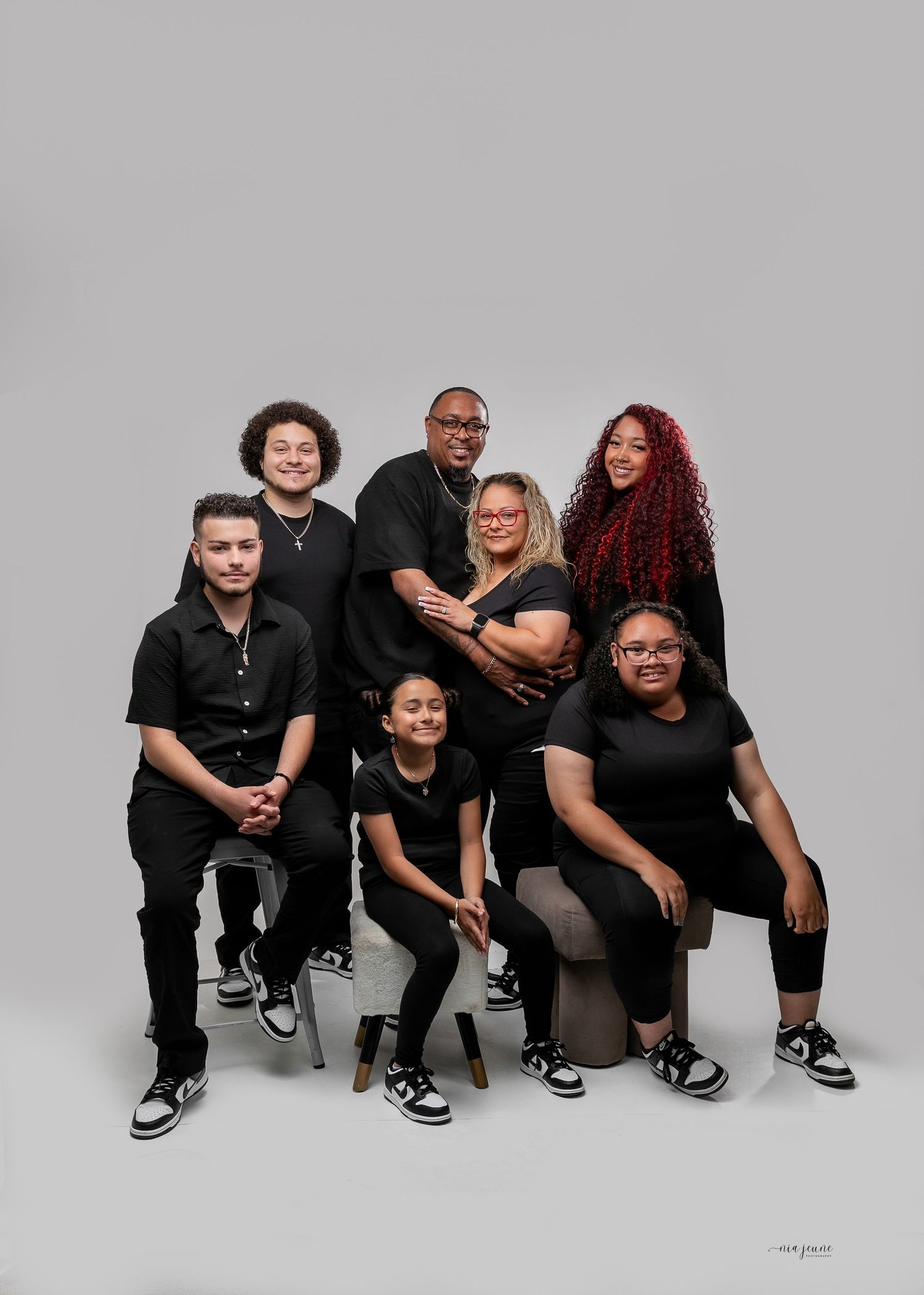 Family of seven posing in coordinated black outfits for a professional studio portrait against a gray background.
