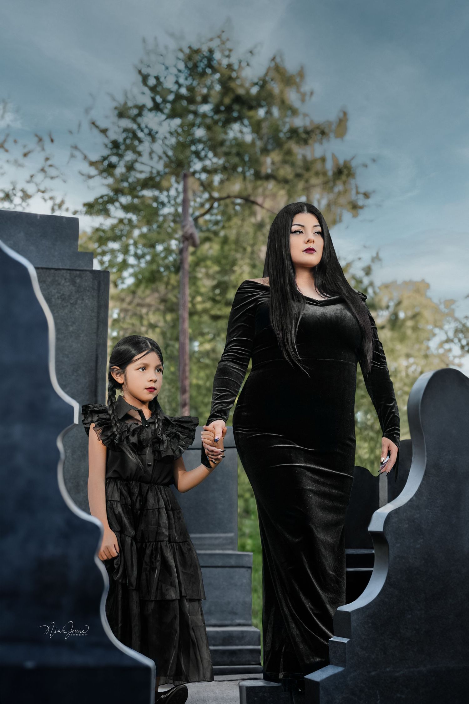 Gothic-inspired portrait with velvet dresses against cemetery backdrop.