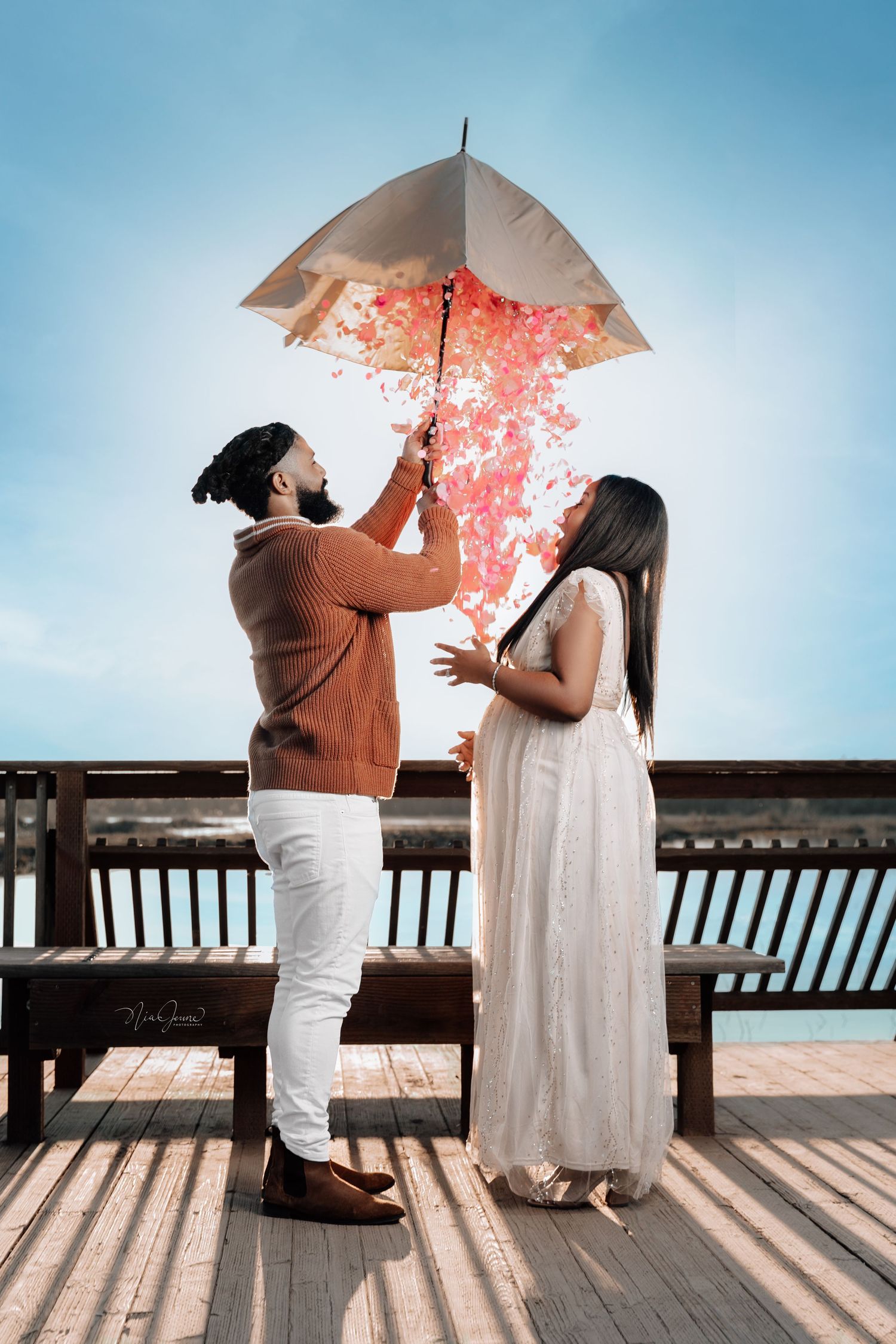 Romantic couple with umbrella on boardwalk creating pink flower effect in sky.